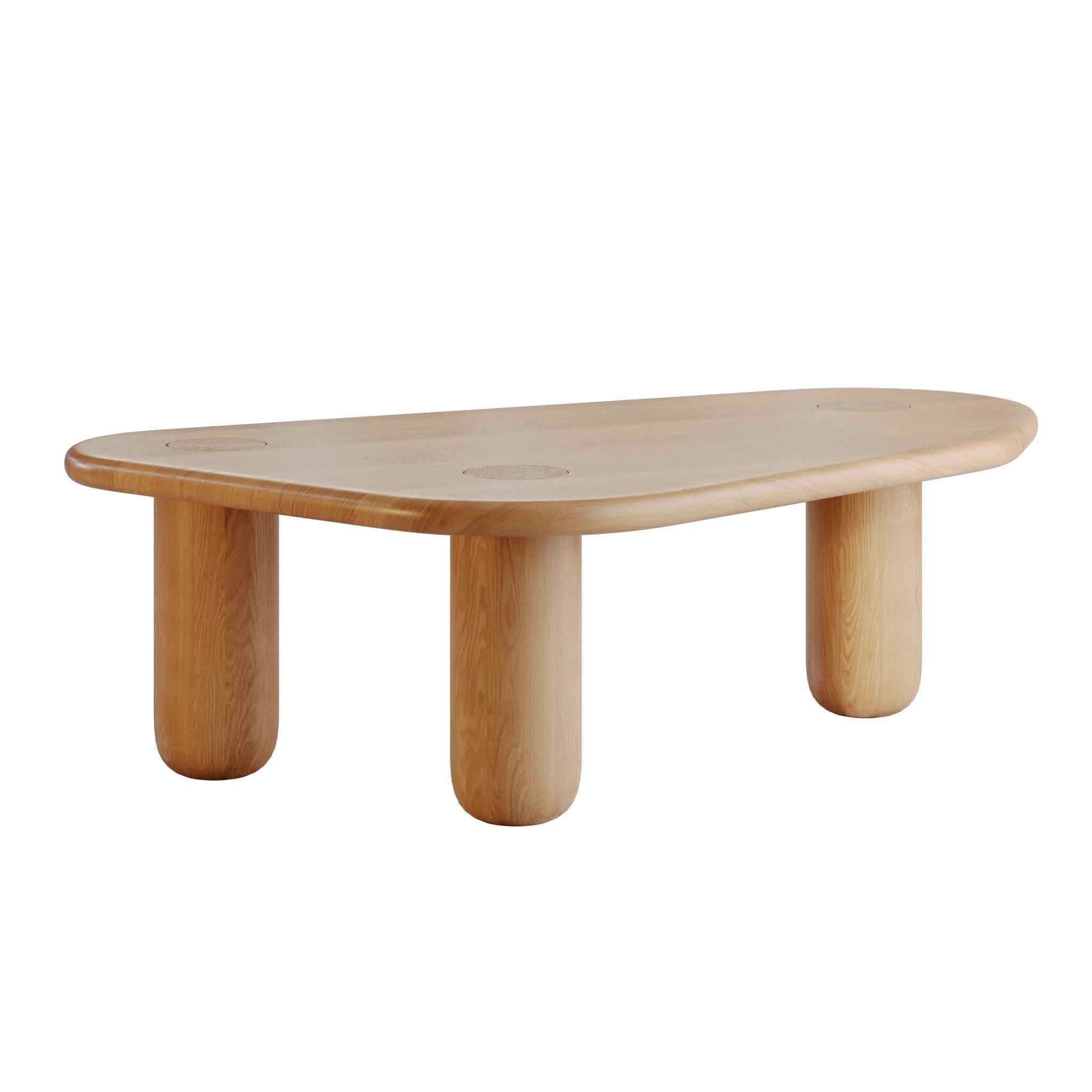 This contemporary coffee table is crafted from solid oak in a natural finish, highlighting the authentic beauty of the wood with its warm tones and expressive grain. The organic design, featuring smooth rounded edges and cylindrical legs, brings a