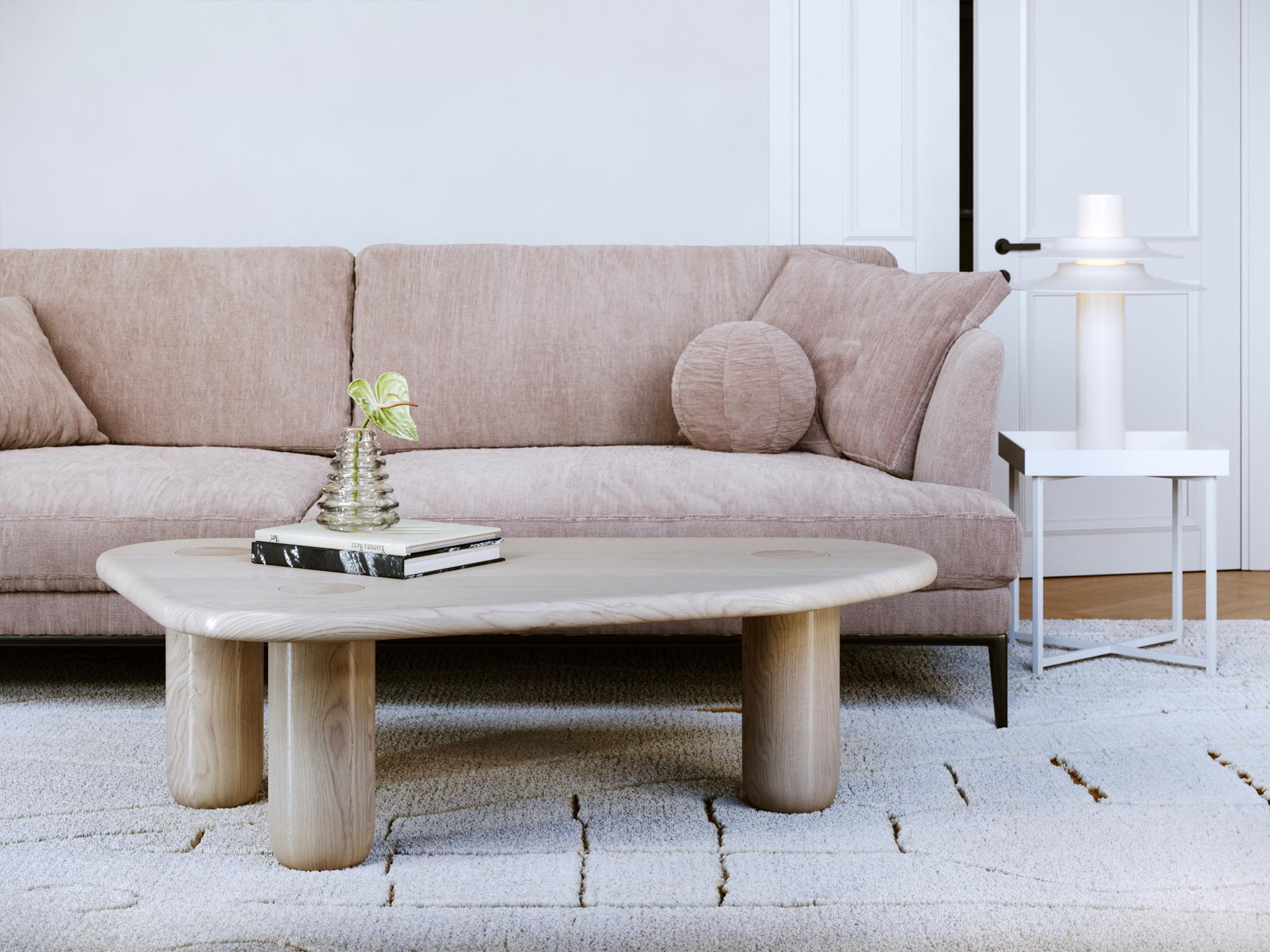 This contemporary coffee table is crafted from solid oak with a refined whitewashed finish that gently softens the natural grain and highlights the organic beauty of the wood. Its flowing form, rounded edges, and cylindrical legs create a sculptural