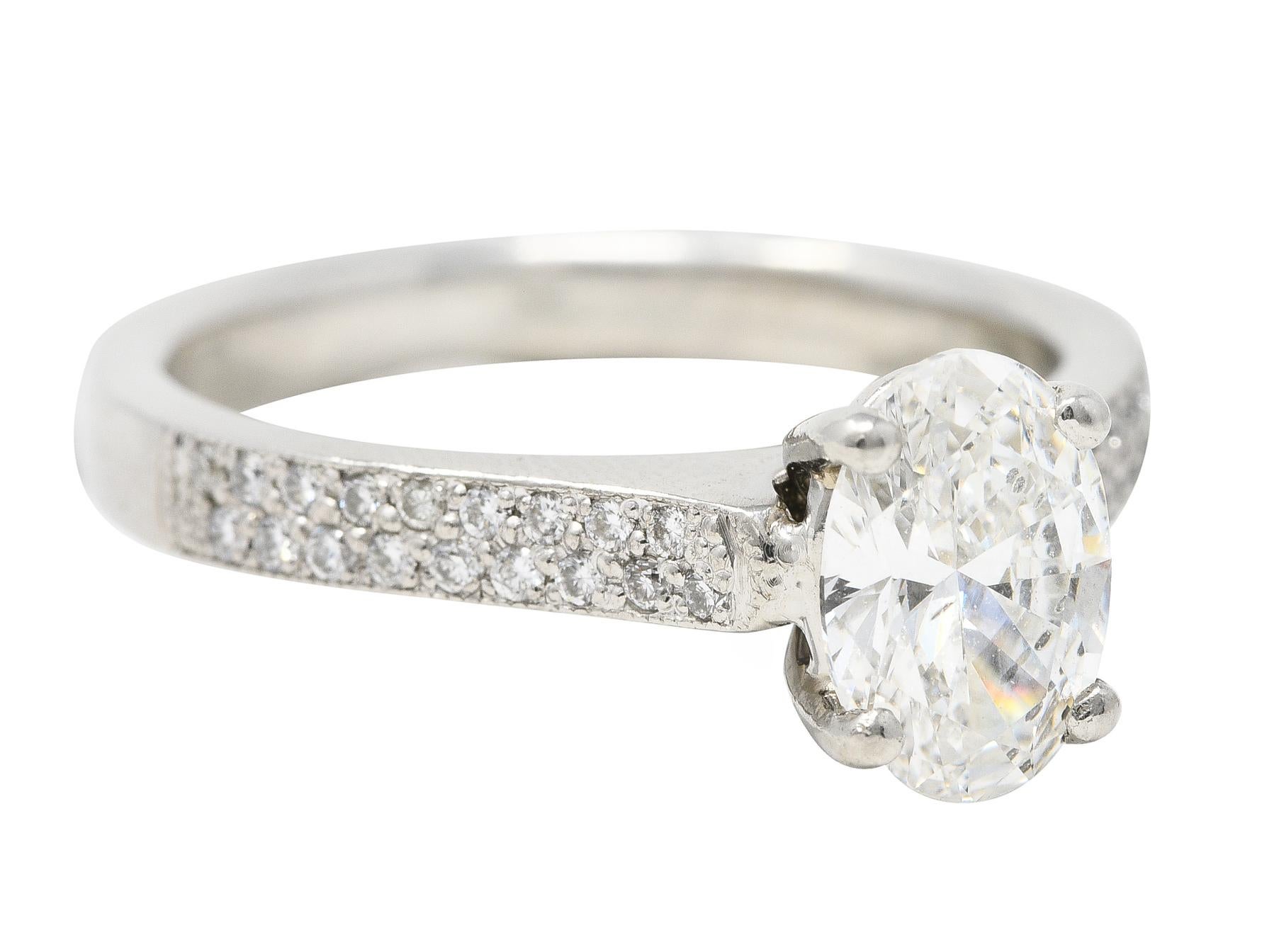 Centering an oval cut diamond weighing 1.08 carats total - F color with SI2 clarity. Prong set and flanked by sleek shoulders set with pavé set round brilliant cut diamonds. Weighing approximately 0.18 carat total - eye clean and bright. Stamped