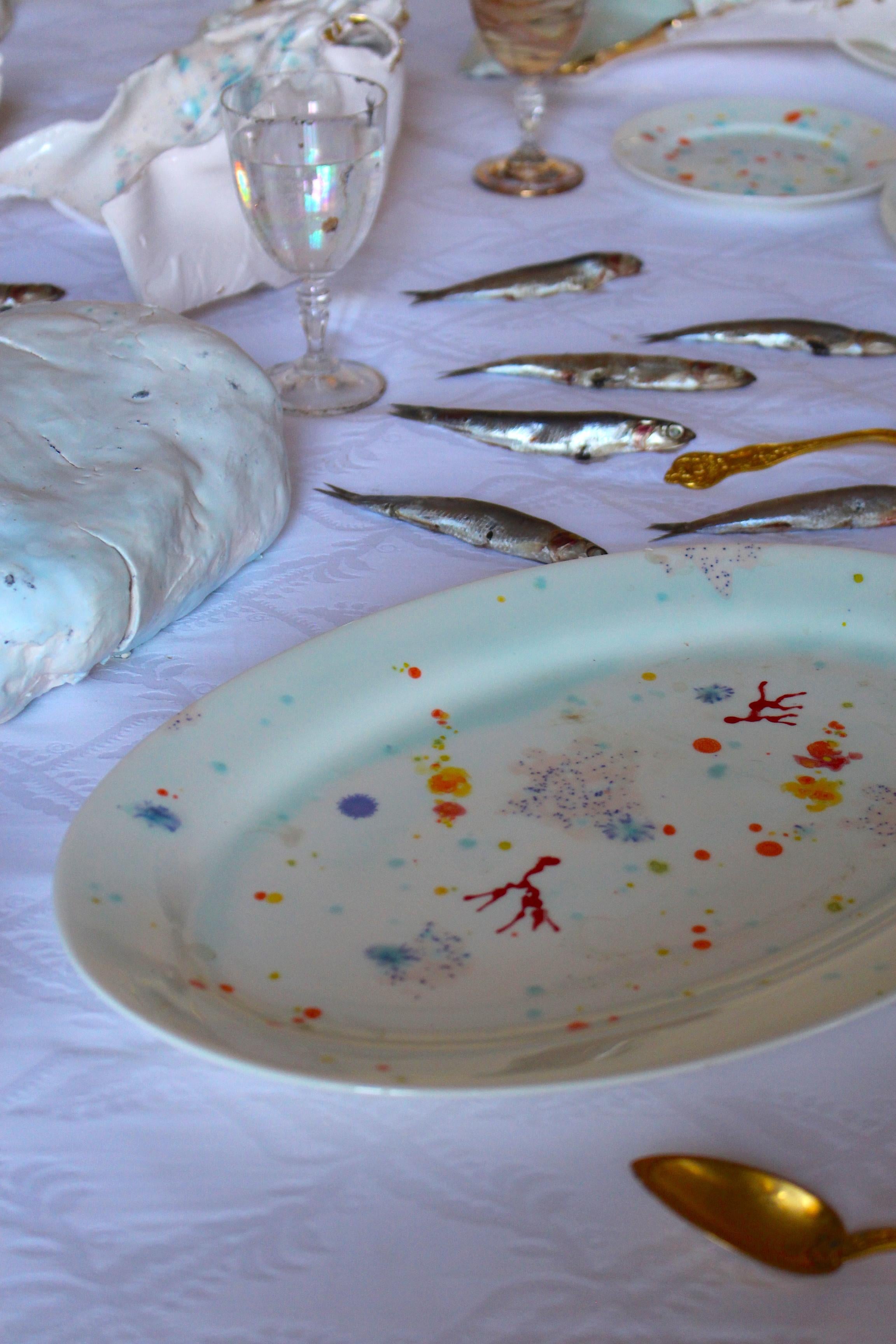 Hecha a mano en Italia con la mejor porcelana, esta fuente ovalada con borde de fondo marino azul tiene corales tumbados sobre un fondo brillante rodeados de misteriosas gemas multicolores que flotan entre pinceladas de arena rosa claro salpicada de
