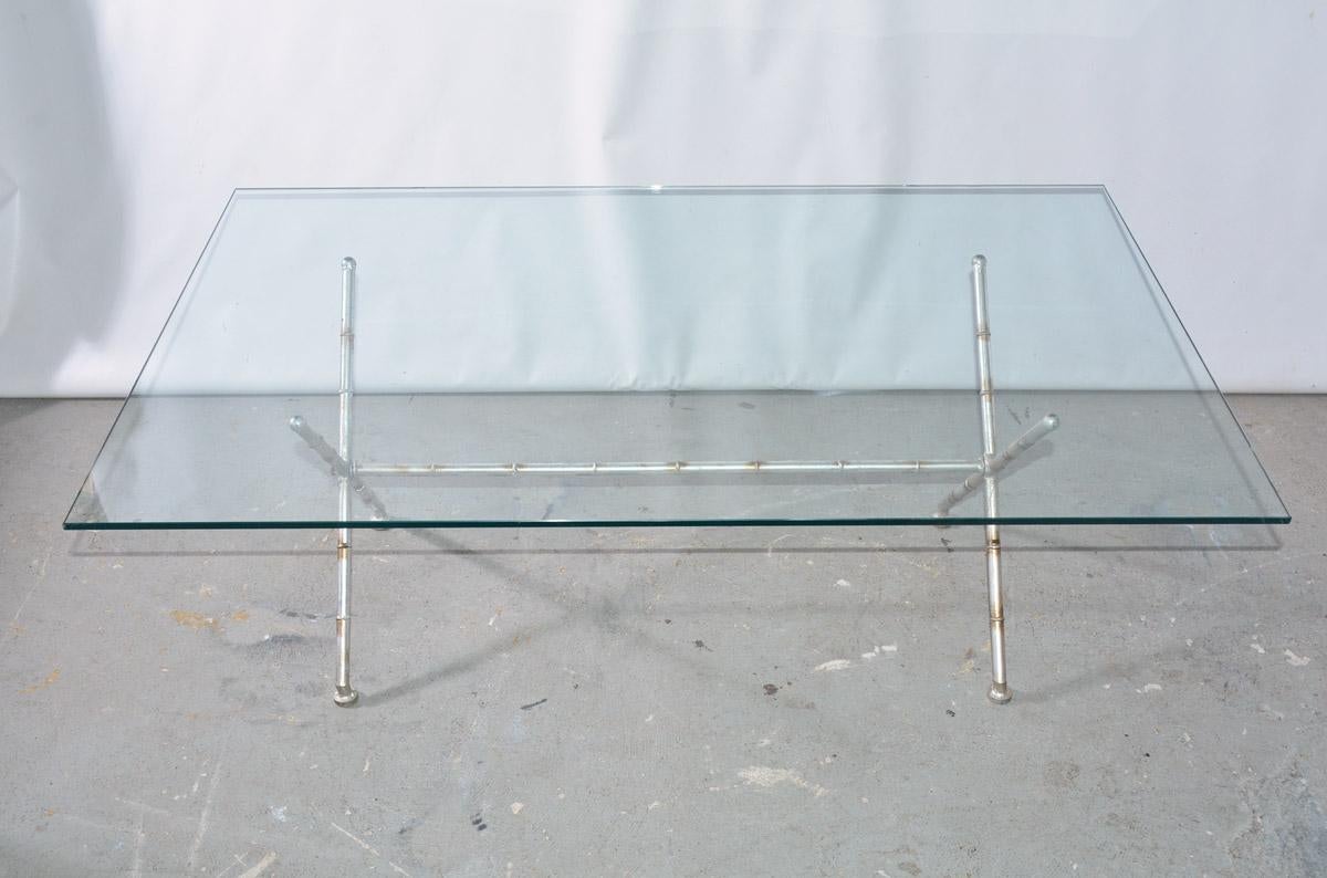 The contemporary coffee table is made of a glass top and faux bamboo metal 