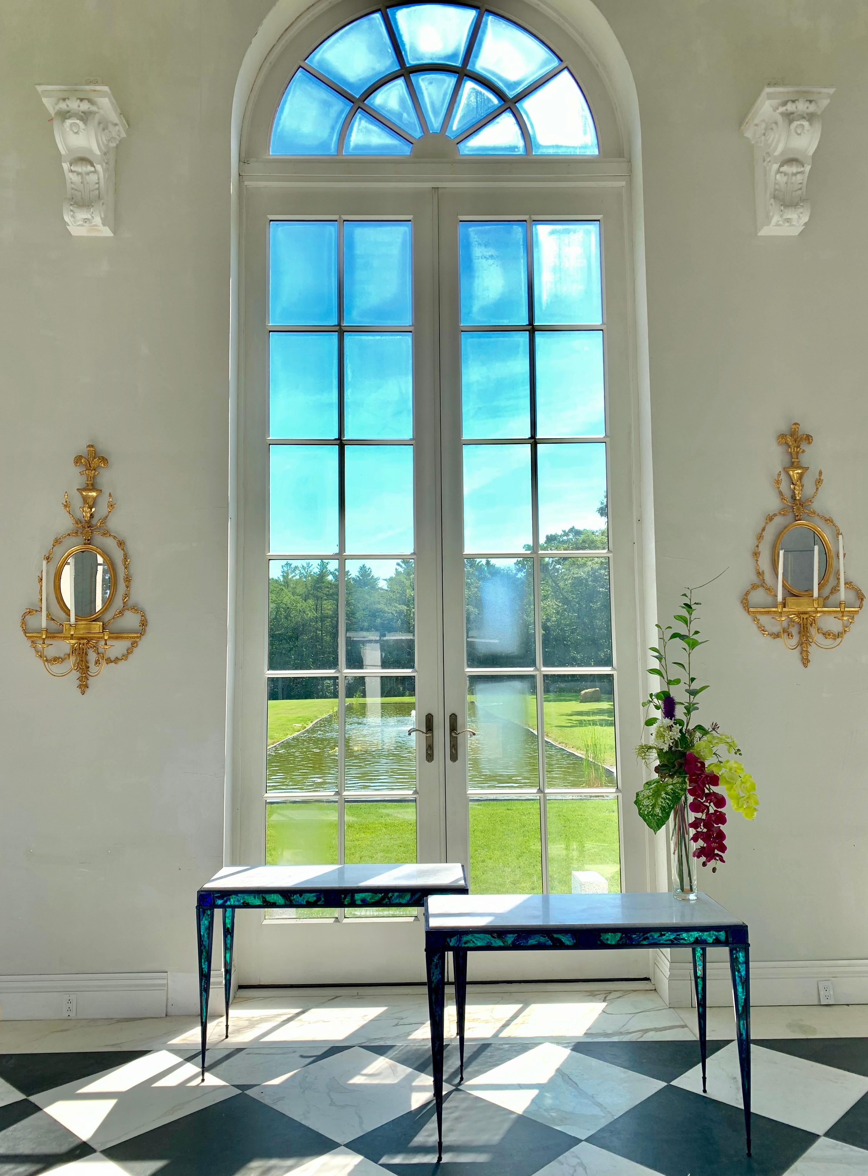 Dom Paragon designed this one of a kind pair of neoclassical inspired console tables.
The handwrought steal frame is powder coated.
The hand blown glass inserts have reverse paint in an abalone color spectrum.
Azur blue, emerald green and