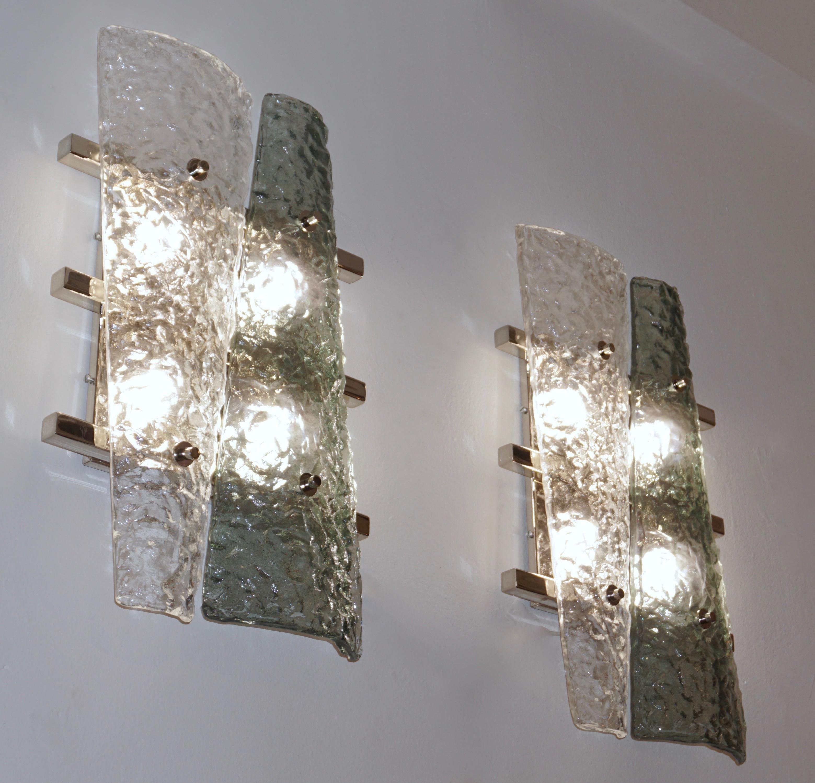 Italian pair of geometric wall lights, entirely handcrafted, the streamlined nickel backplate consisting of a series of 3 horizontal nickel bars supports 2 destructured triangular elements in crystal and aquamarine green Murano glass presenting a