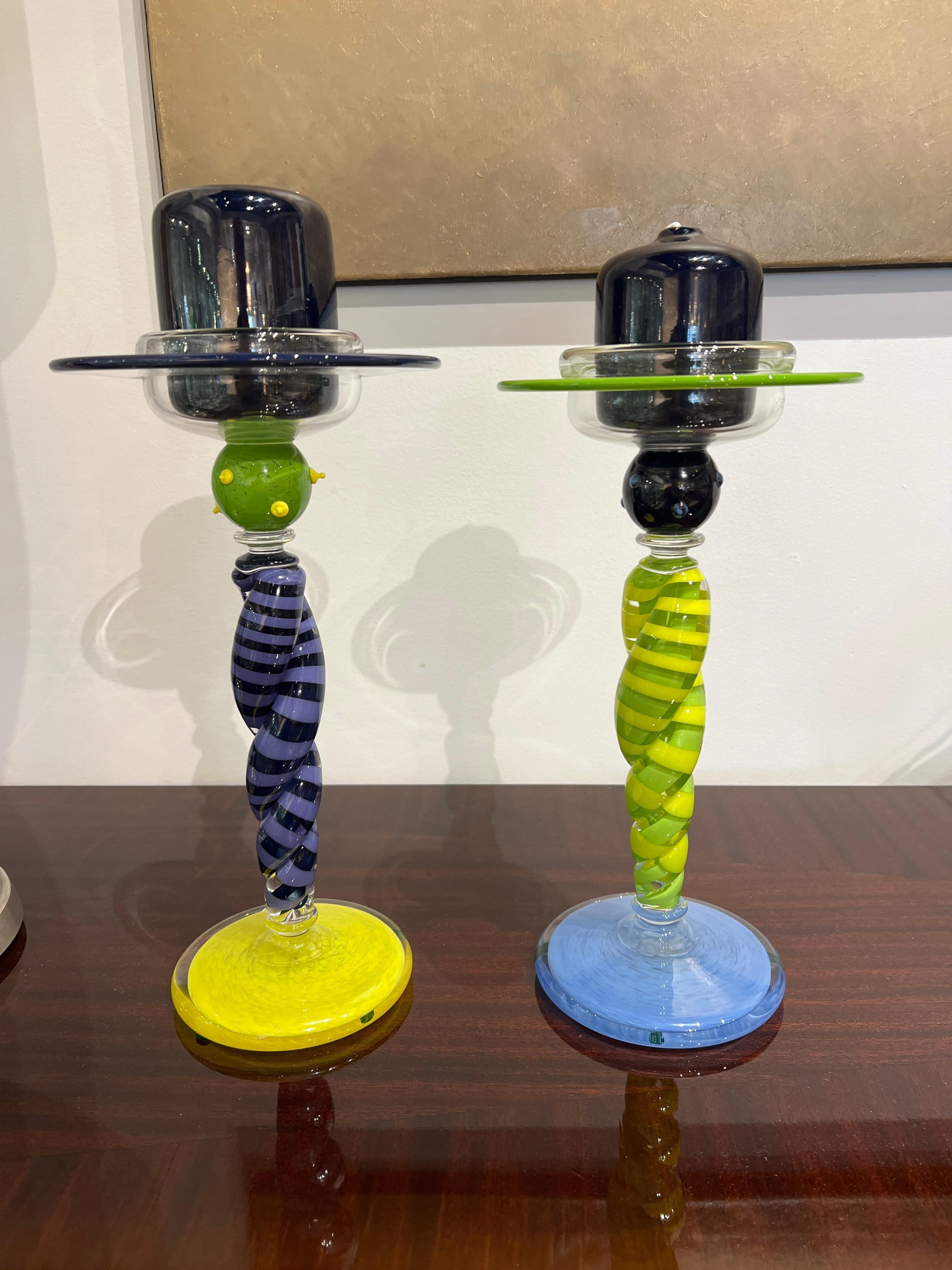 Paire de chandeliers contemporains en verre aux couleurs vives de l'arbre (violet, bleu, vert et jaune) et du pied jaune.  Le pilier de bougie en verre est de couleur noire.

Signature : Cray