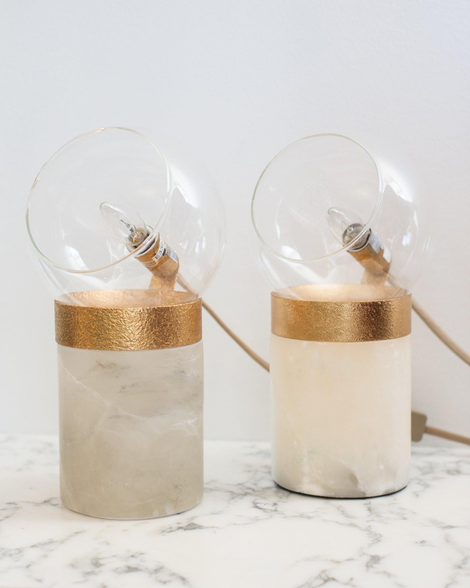 A pair of small lamps on solid quartz bases with glass domes and brass details. Suitable for a desk, night stands or end tables, these lamps are most beautiful when used with Edison bulbs. When lit, the translucent quartz is partially illuminated,
