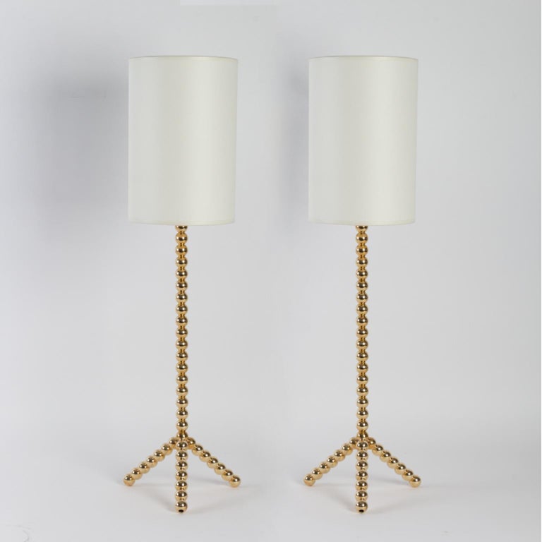 Pair of fancy table lamps, in gilded solid brass beads.

Composed of a stem resting on a tripod base on which are threaded one by one solid gold brass balls in the manner of a pearl necklace. 
They are dressed with a cylindrical lampshade in