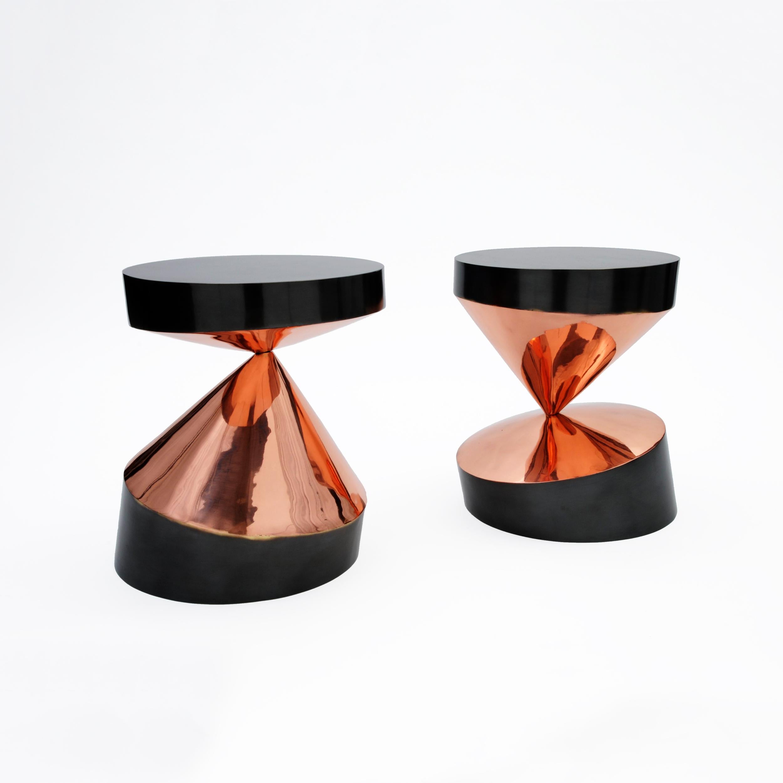 Whirling Twins - Bronze

'Whirling Twins' are a pair of small sculptural tables where two cones balancing on their tips maintain a perfectly horizontal plane in burnished brass.
The red cones in polished copper reflect flames of warm and vibrant