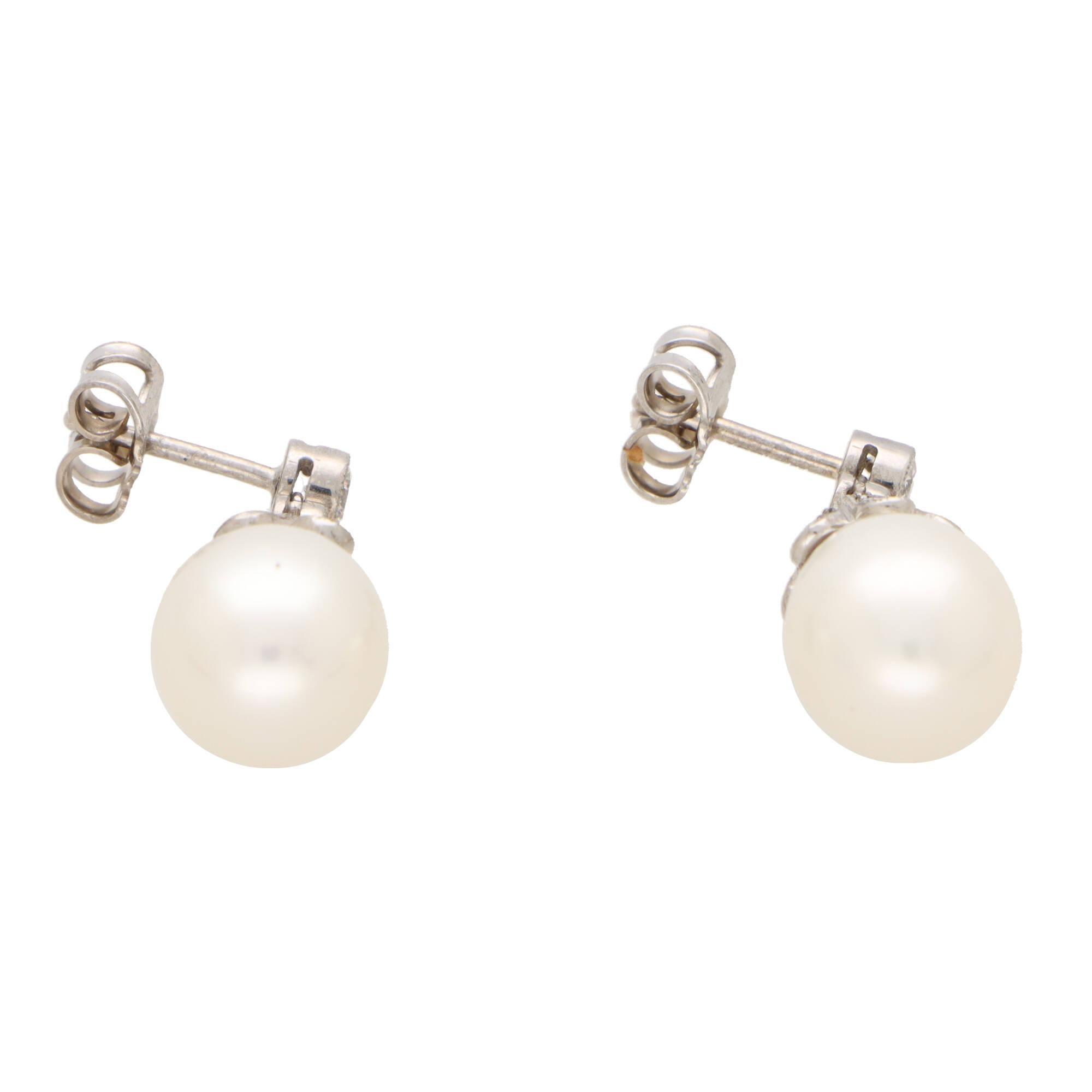 A beautiful pair of white cultured pearl and diamond drop earrings set in 18k white gold.

Each earring is firstly composed of a rub over round brilliant cut diamond stud, secured to reverse with a post and butterfly fitting. Hanging freely from the