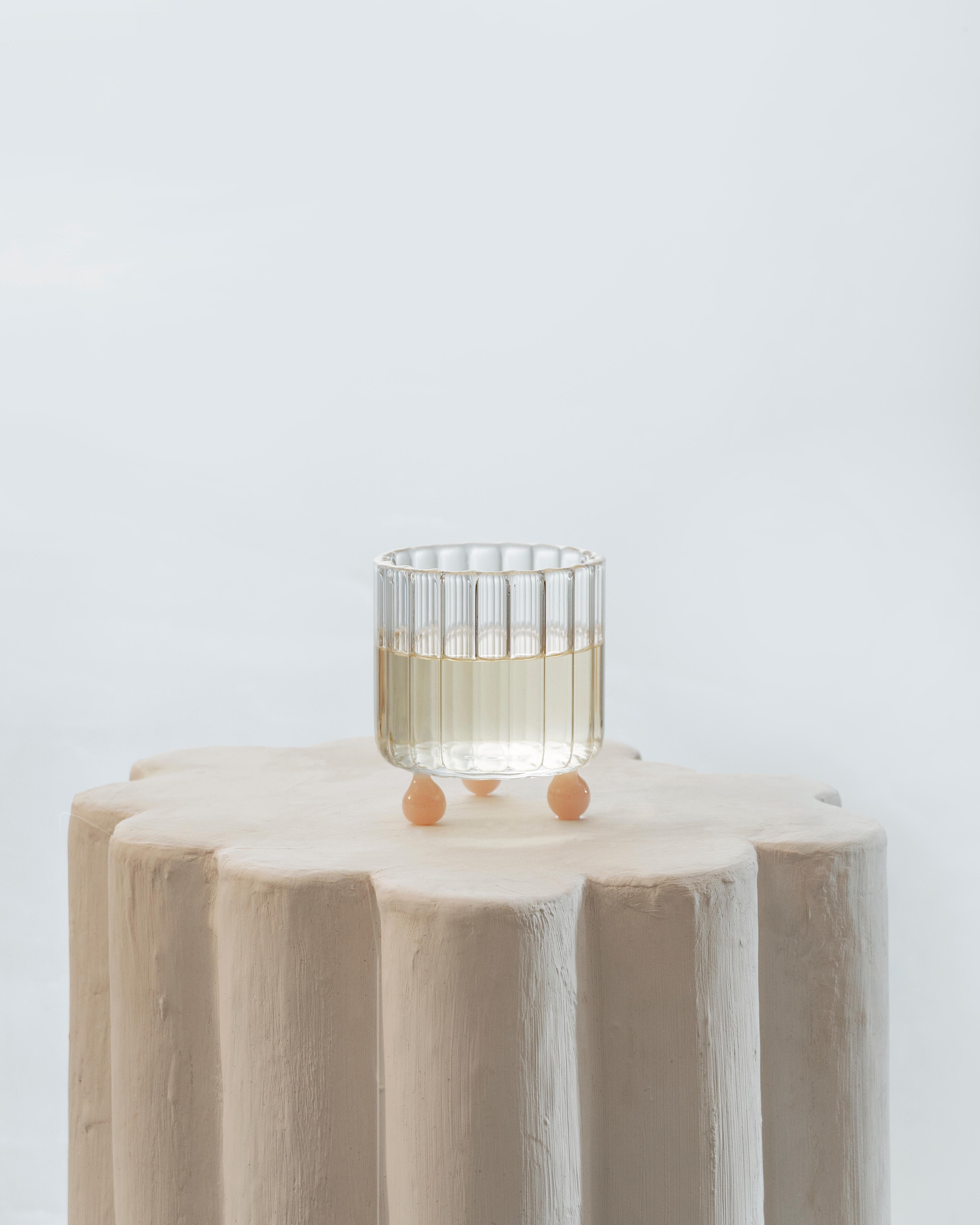 A lowball glass of an atypical shape, inspired by Postmodern architecture. Each piece is handmade in Italy by Master glassblowers, using high-quality borosilicate glass. The ribbed glass body rests on top of three clear spheres, playfully elevating