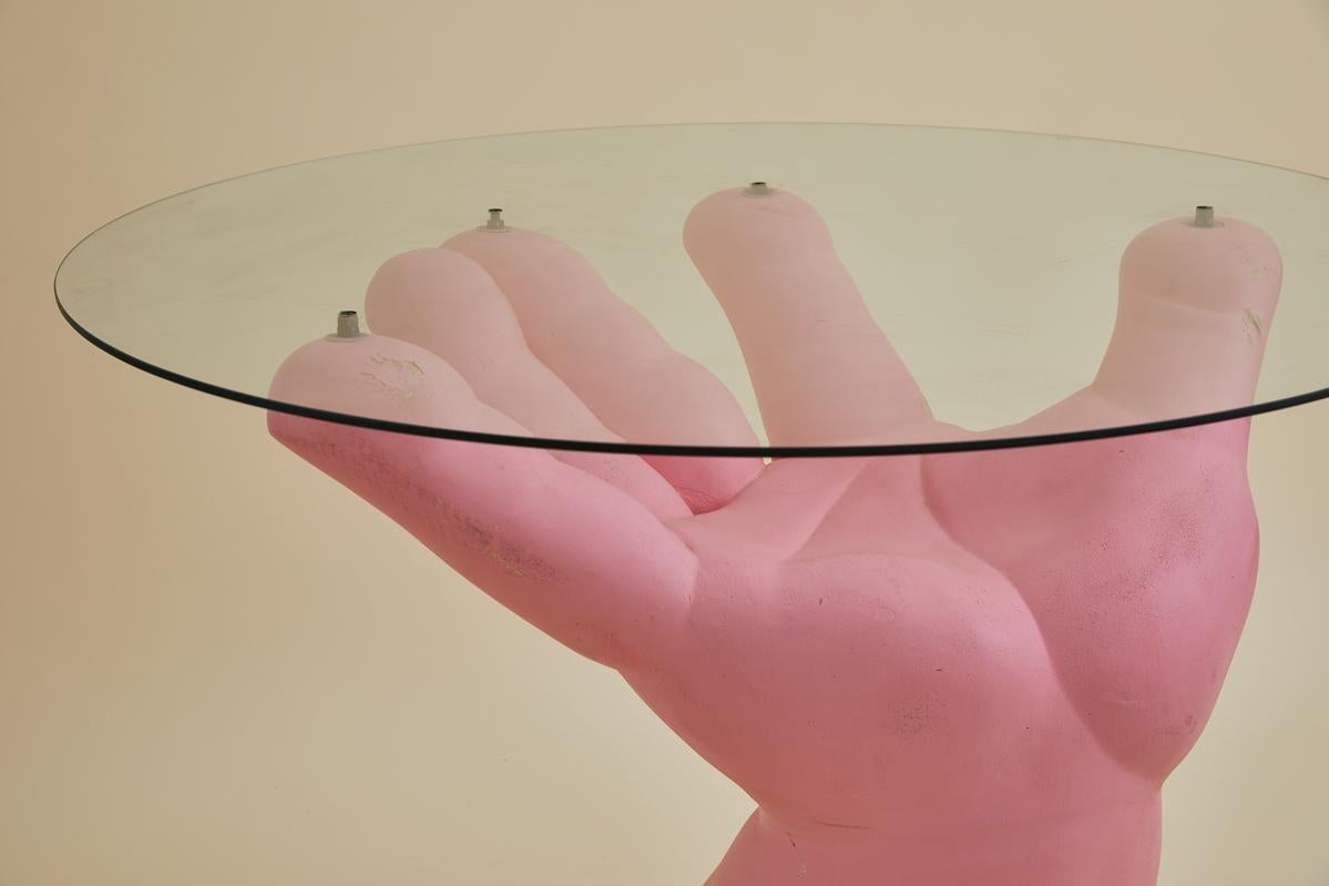 Cette table d'appoint sculpturale postmoderne du 20e siècle est une pièce qui attire l'attention. La base, en forme de main rose ouverte, dégage une esthétique ludique et surréaliste, qui rappelle les influences du surréalisme et du pop art.
