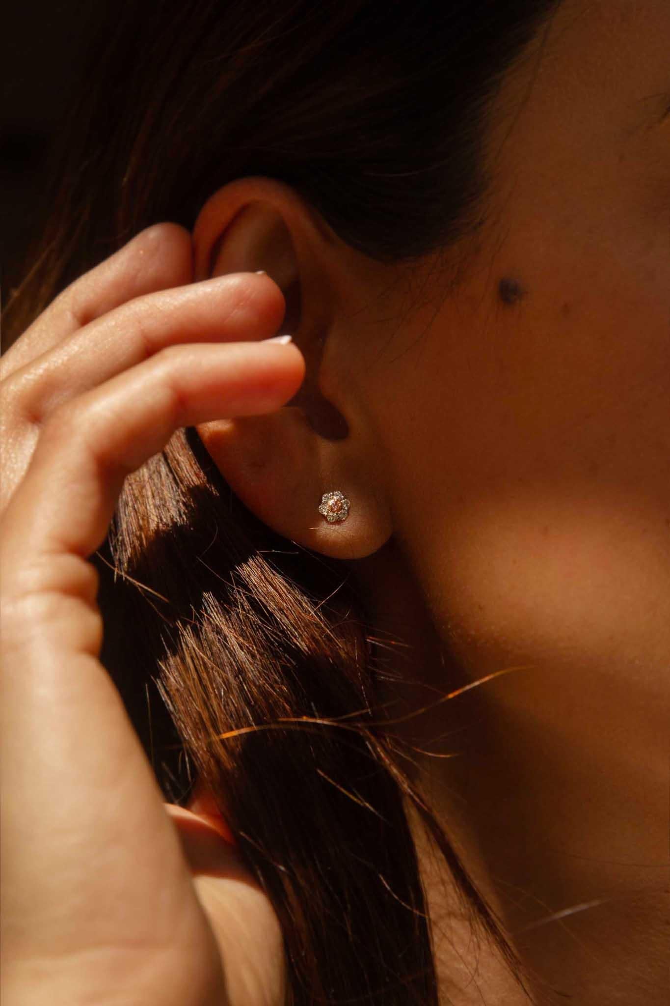 A petal bloom of diamonds bright,
A pink heart shines, a radiant sight.
In rosy gold, a precious pair,
A floral dream, beyond compare.

The 18 carat white gold Turia Earrings each hold a Fancy Purplish-Pink diamond in a rose gold setting and with a
