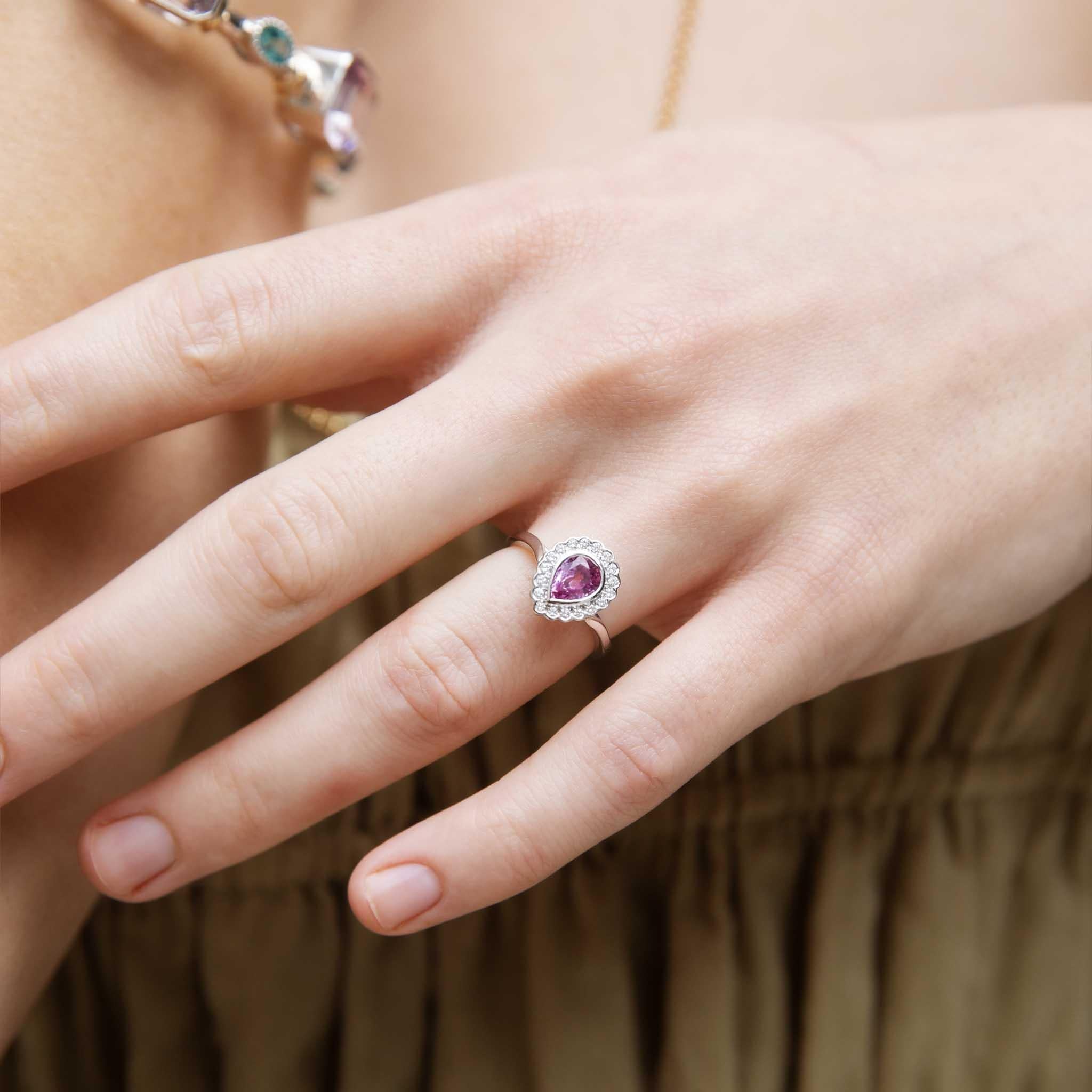 Dolcemente realizzato in oro bianco 18 carati, l'anello Priya è una vera delizia.  Il suo zaffiro rosa-viola a forma di pera è incastonato in un'aureola di pizzo impreziosita da diamanti.  Un modo affettuoso per chiedere di condividere la vita con