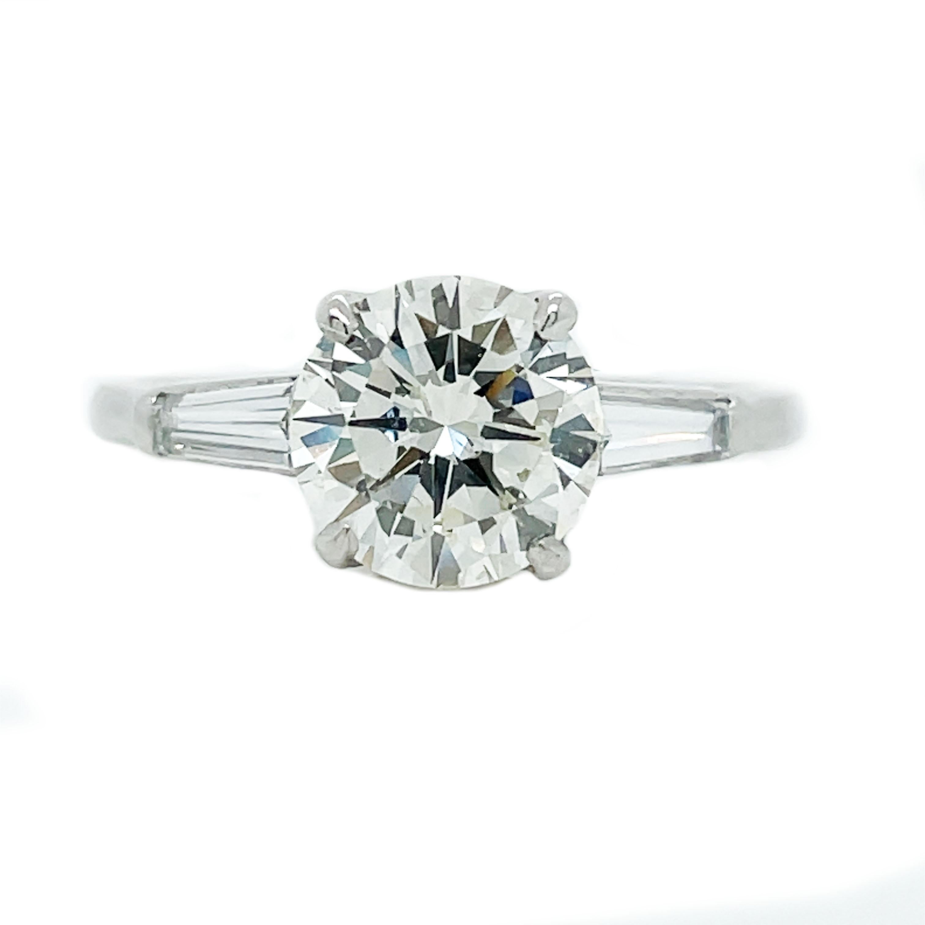 This is an absolutely killer platinum engagement ring showcasing a bright and lively center diamond complimented by gorgeous baguette diamonds! A stunning, slightly yellow, and sparkling round diamond, weighing 2.01 carats, is tastefully presented