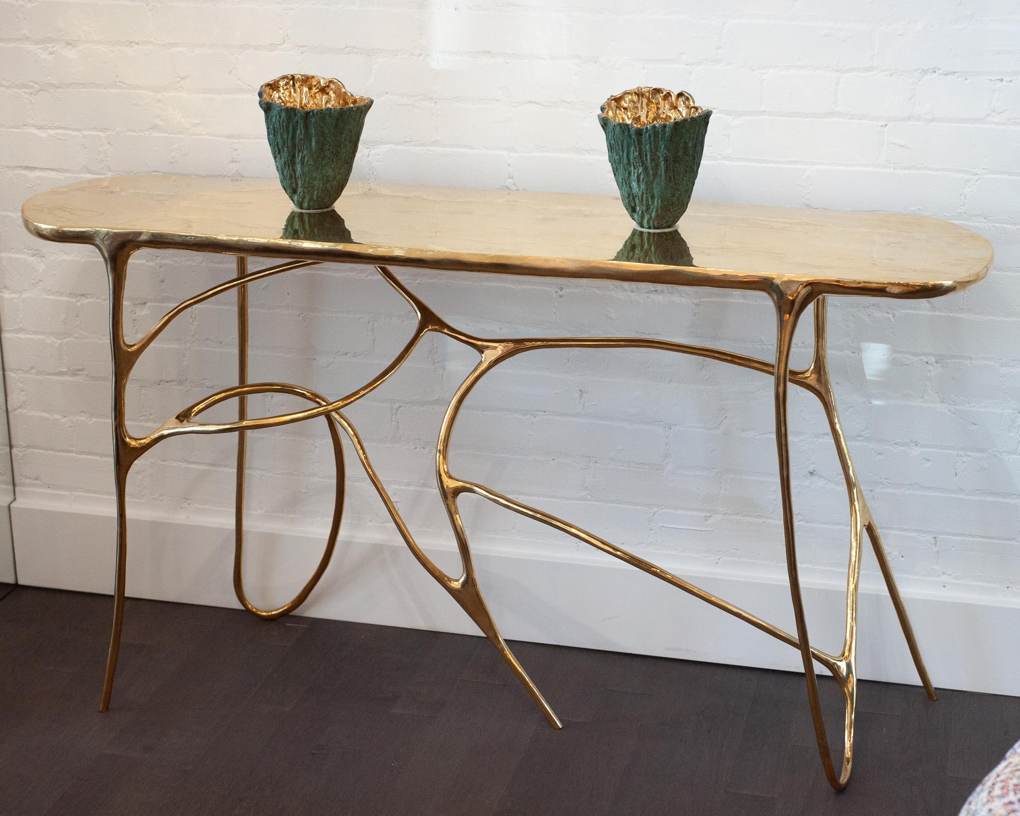 Console sculpturale en laiton - Cette console, entièrement coulée en laiton poli, se distingue à la fois par sa forme et par son matériau. Son plateau solide repose sur une base dynamique aux lignes sculpturales et tourbillonnantes, où le mouvement