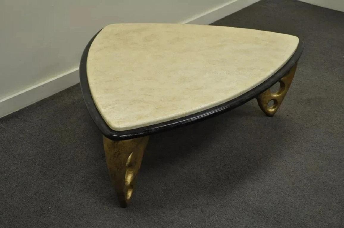 Postmoderner skulpturaler dreieckiger Couchtisch mit Kunstmarmorplatte. Das Möbelstück hat eine cremefarbene Platte aus Kunstmarmor auf einem Sockel aus schwarzem Kunstmarmor mit drei goldfarbenen, skulpturalen Beinen in Notlage. Sehr einzigartig