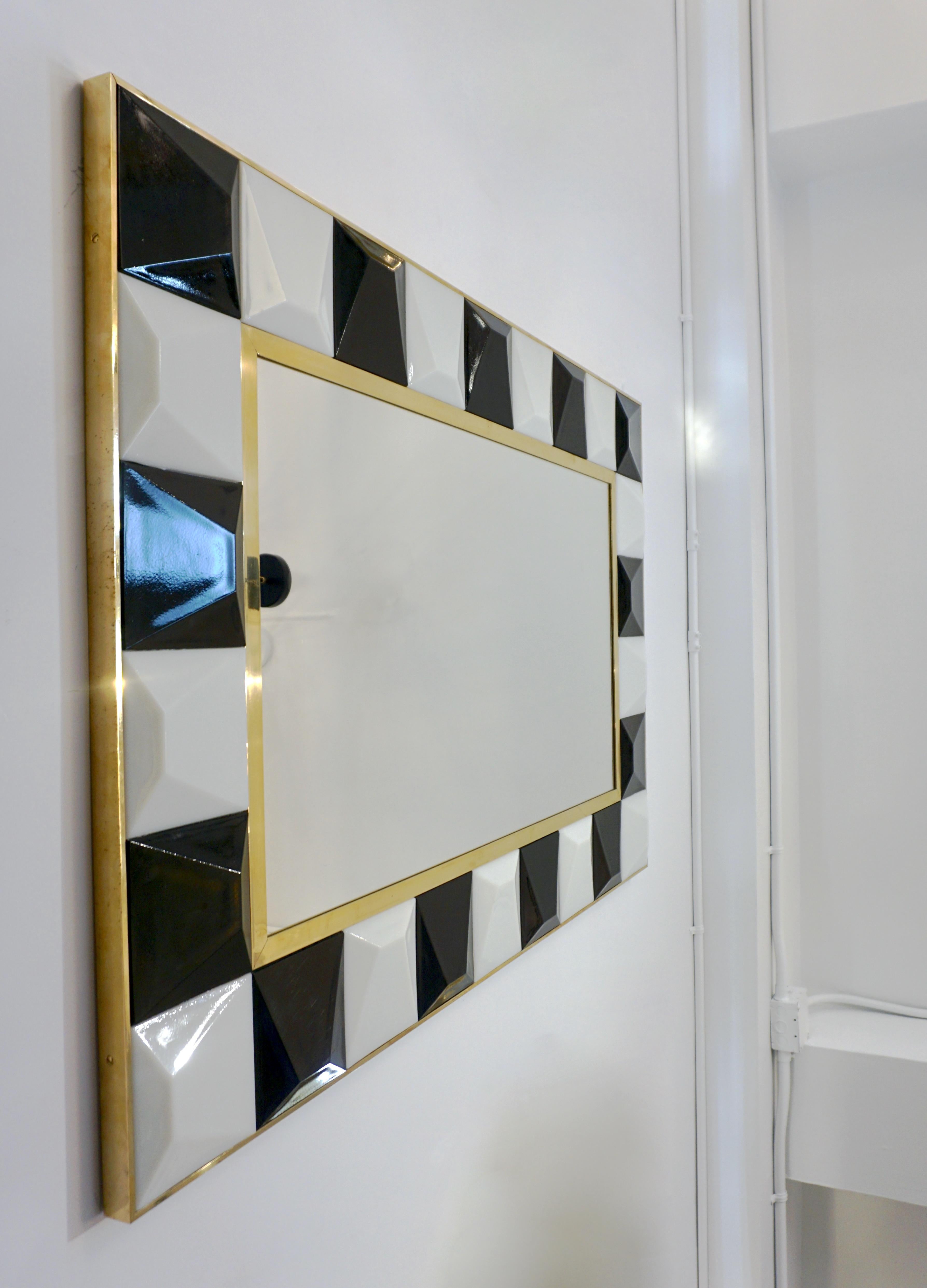 A rectangular mirror entirely handcrafted in Italy, the geometric design composed of squares in black and white Murano glass encased in a handmade brass frame, each square glass element with a raised diamond cut surface that makes this creation