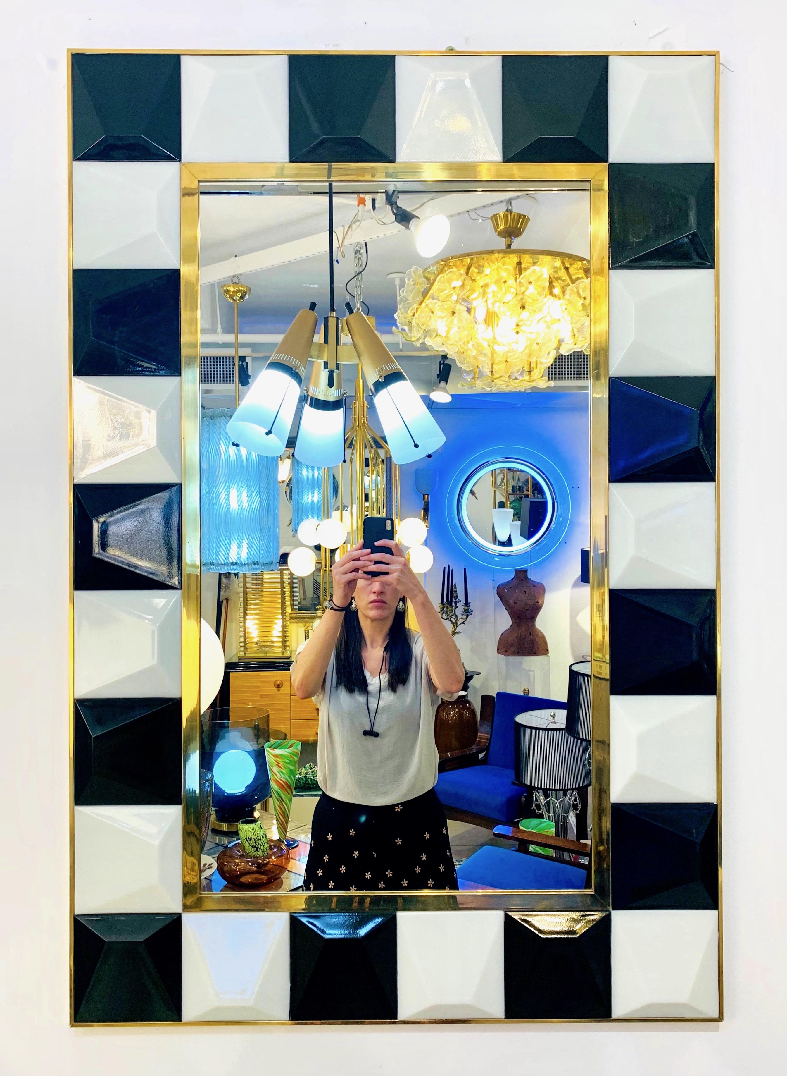 A rectangular mirror entirely handcrafted in Italy, the geometric design composed of squares in black and white murano glass encased in a handmade brass frame, each square glass element with a raised diamond cut surface that makes this creation