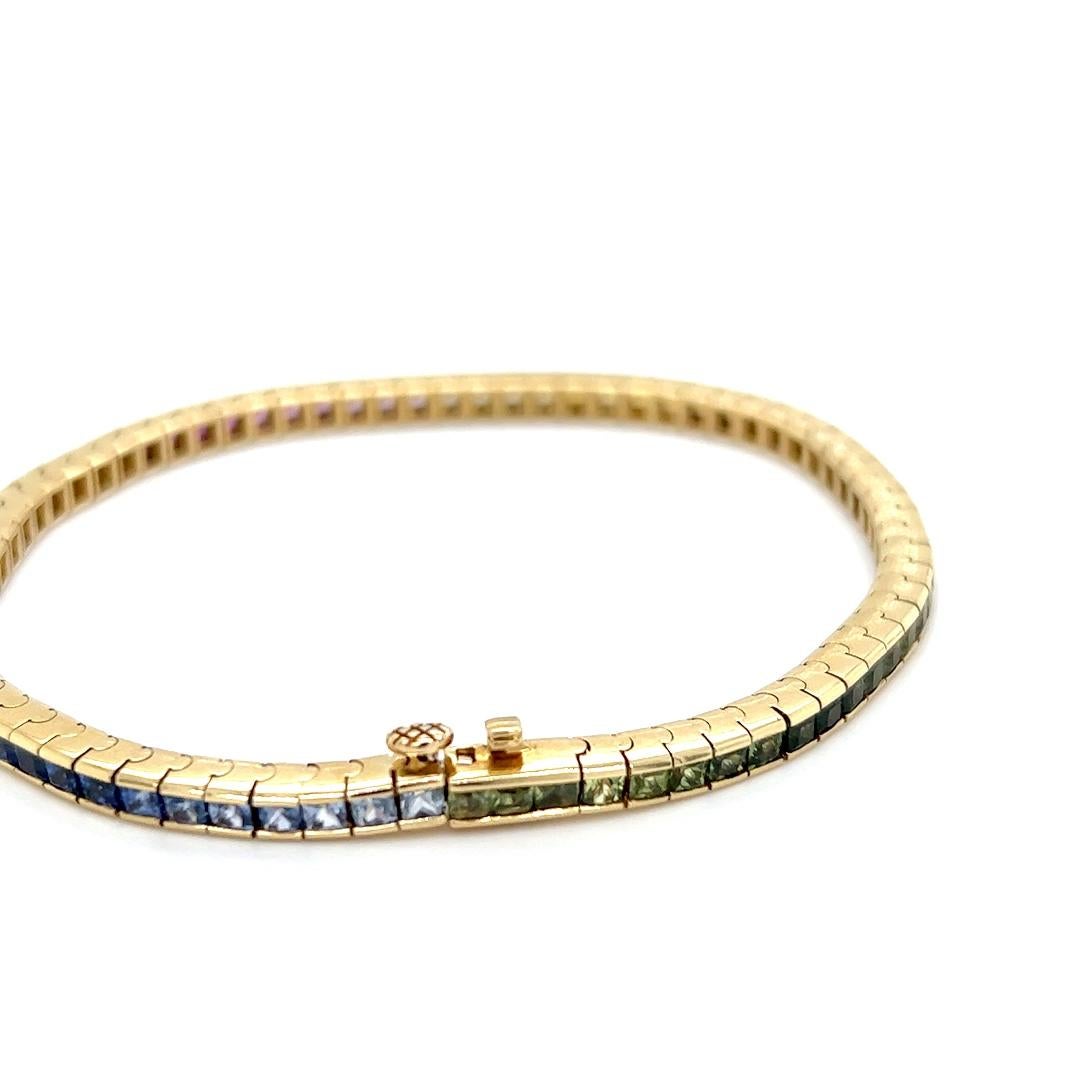 One 18 karat yellow gold line bracelet set with seventy-four (74) princess cut rainbow colored sapphires, approximately 7.28 carat total weight.  The bracelet measures seven inches long and is complete with a box closure and safety clasp. The
