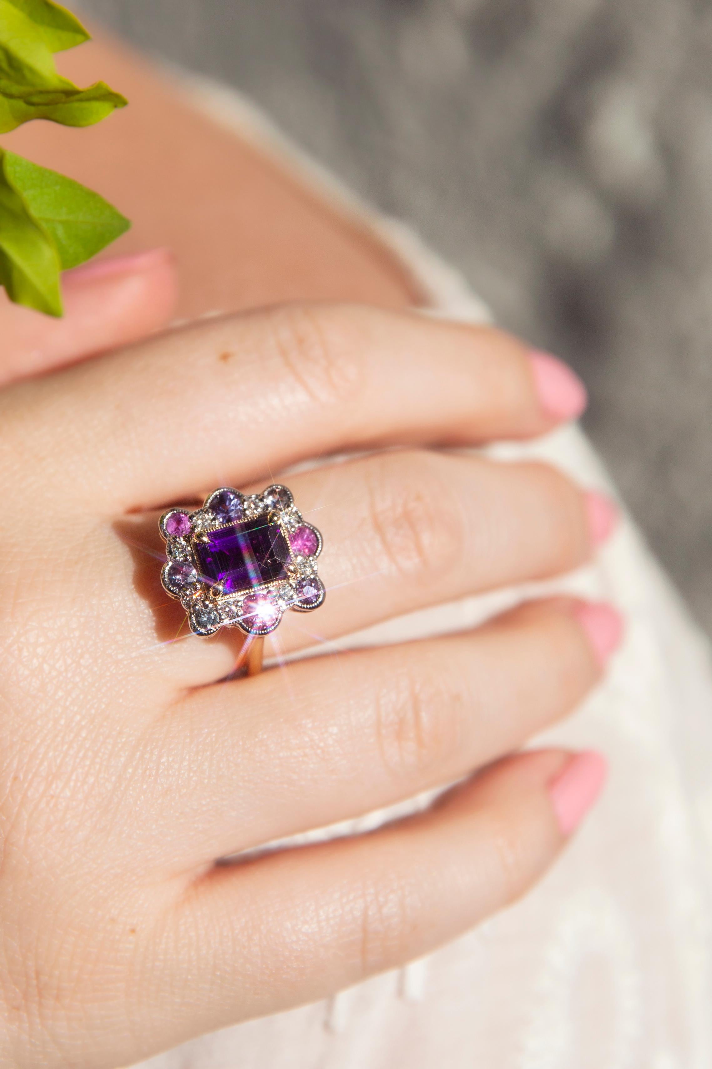 Forged in 18 carat gold, this stunning contemporary ring is a diverse light show of radiant colour. A gorgeous emerald cut vivid purple amethyst rests in a yellow gold setting with a white gold border of sapphires ranging in colour from pink and