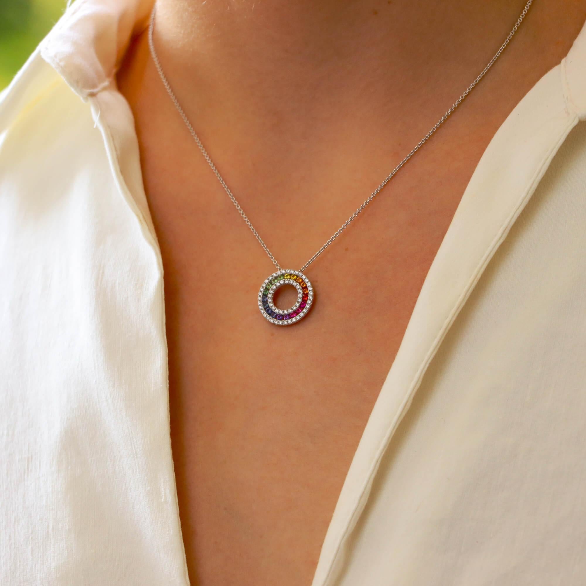 An elegant rainbow sapphire and diamond circle pendant set in 18k white gold.

The pendant depicts a circle motif, centrally set with a ring of round cut rainbow sapphires. These sapphires are bordered by round brilliant cut diamonds which enhance