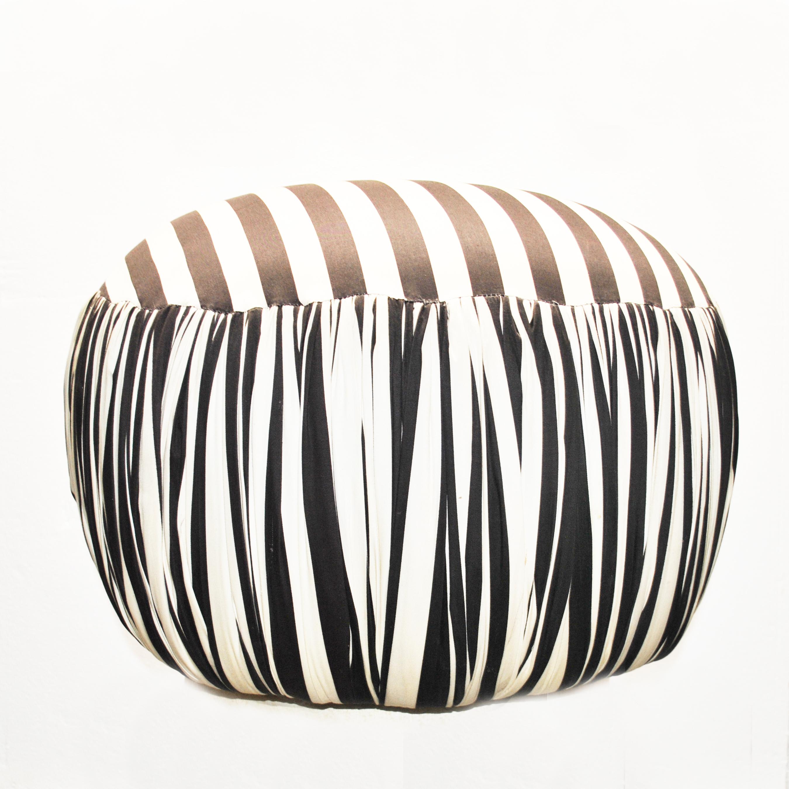 A round contemporary pouf or ottoman in black and white striped fabric with pleated sides.