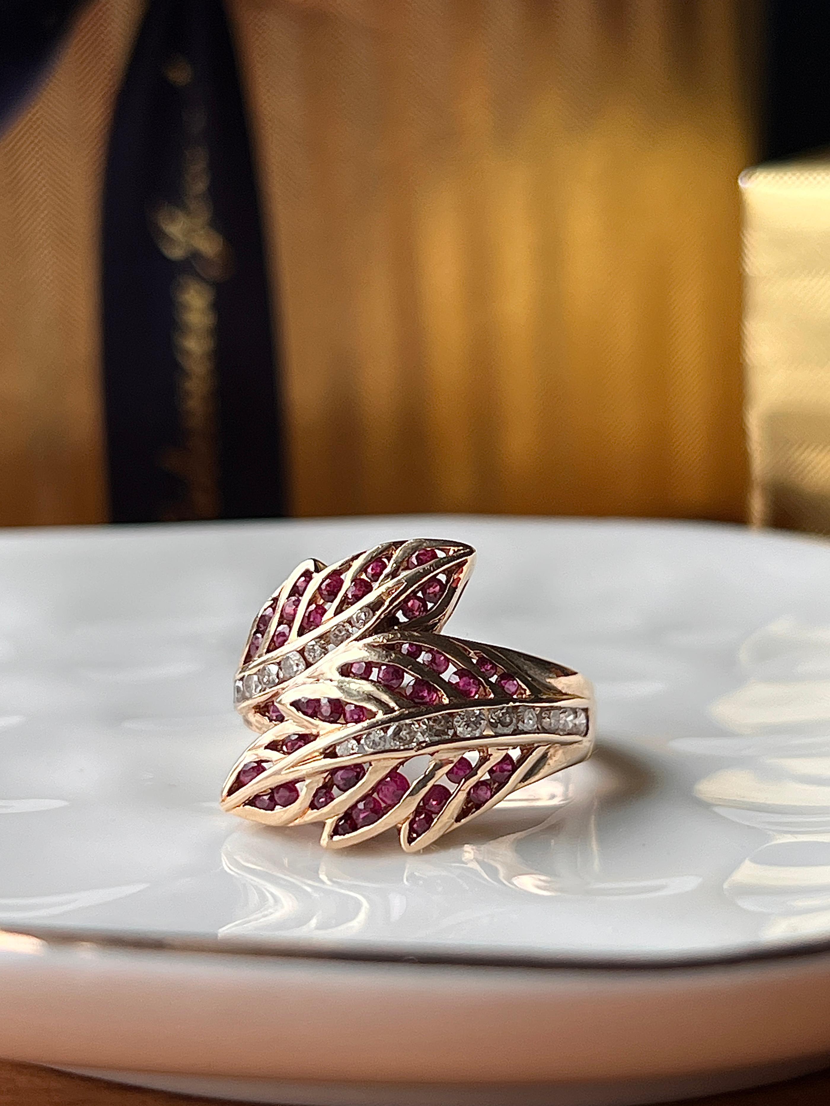 Ein Bypass-Blattring aus 14 Karat Gelbgold aus den 1980er Jahren, besetzt mit achtunddreißig runden Rubinen mit einem Gesamtgewicht von etwa 0,84 Karat. Das Design wird durch neunzehn runde Brillanten von insgesamt ca. 0,46 Karat mit der Farbe J-K