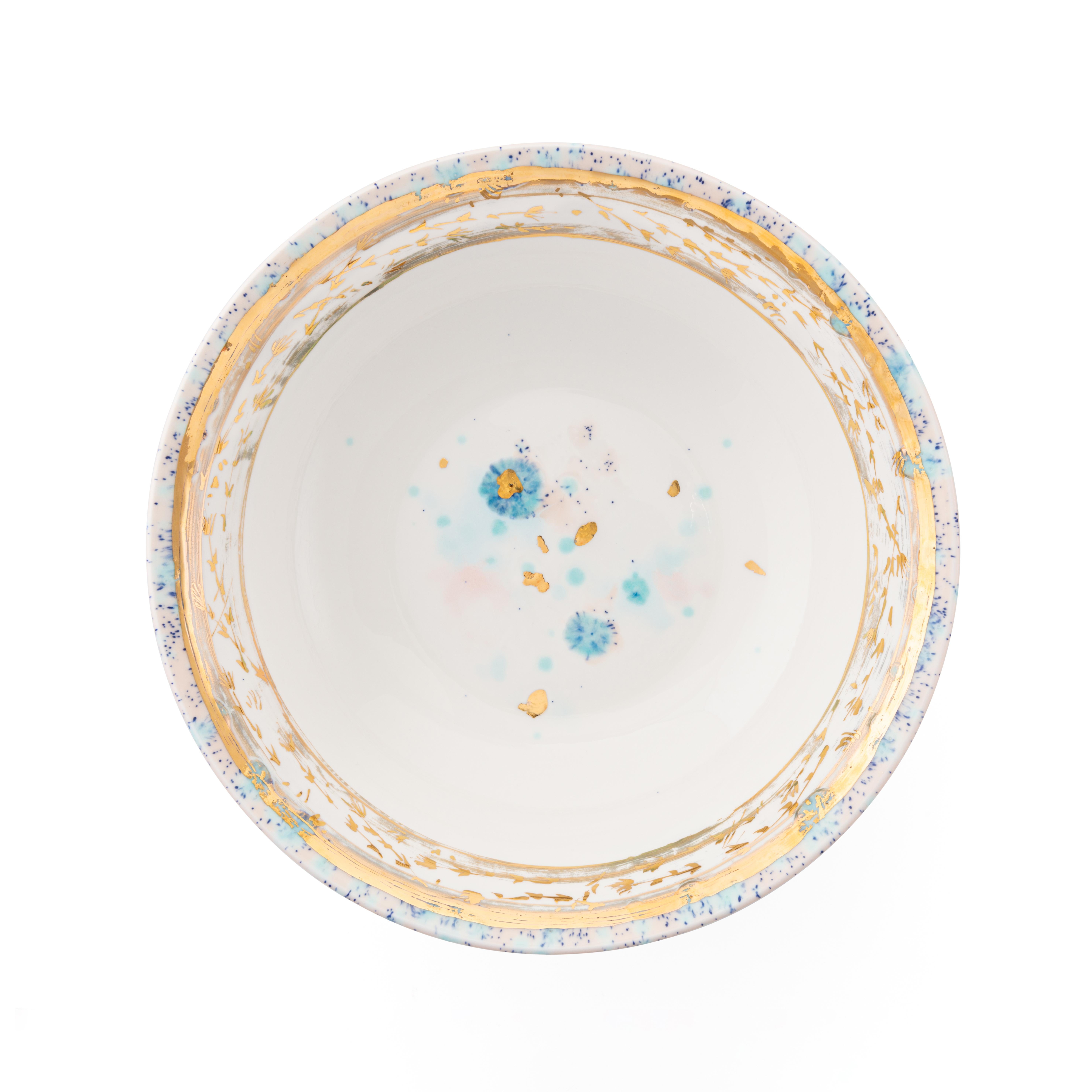 Peint à la main en Italie à partir de la porcelaine la plus fine, ce saladier Dafne présente un étroit bord à pois roses et bleus entourant un large et délicat décor doré de fleurs stylisées. De subtils pinceaux bleu clair et rose saupoudrés de