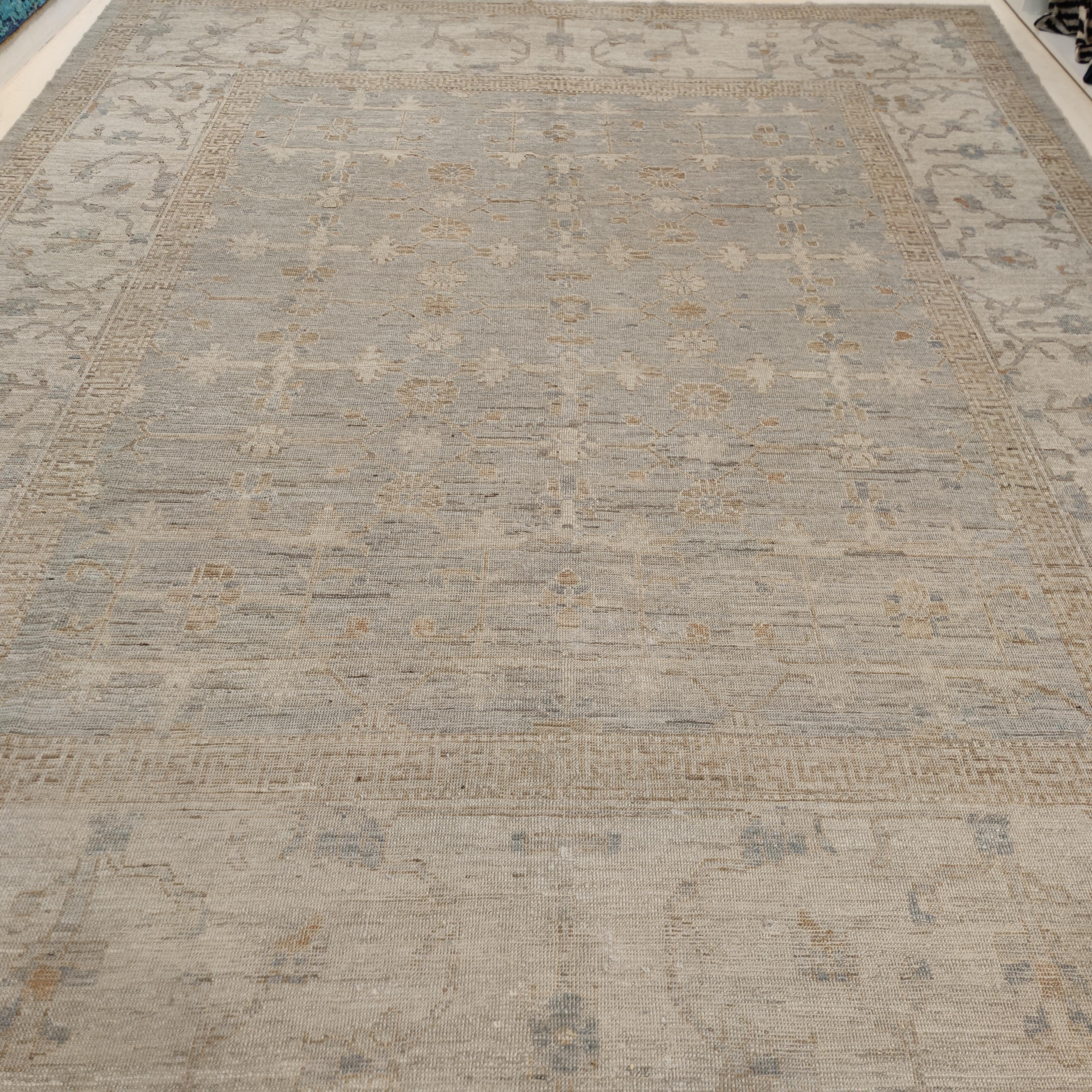 Noué à la main avec de la laine fine et lustrée des hauts plateaux afghans de Ghazni, cet élégant tapis se distingue par un réseau de palmettes stylisées disposées en une répétition infinie sur un fond gris/beige clair très doux. La large bordure