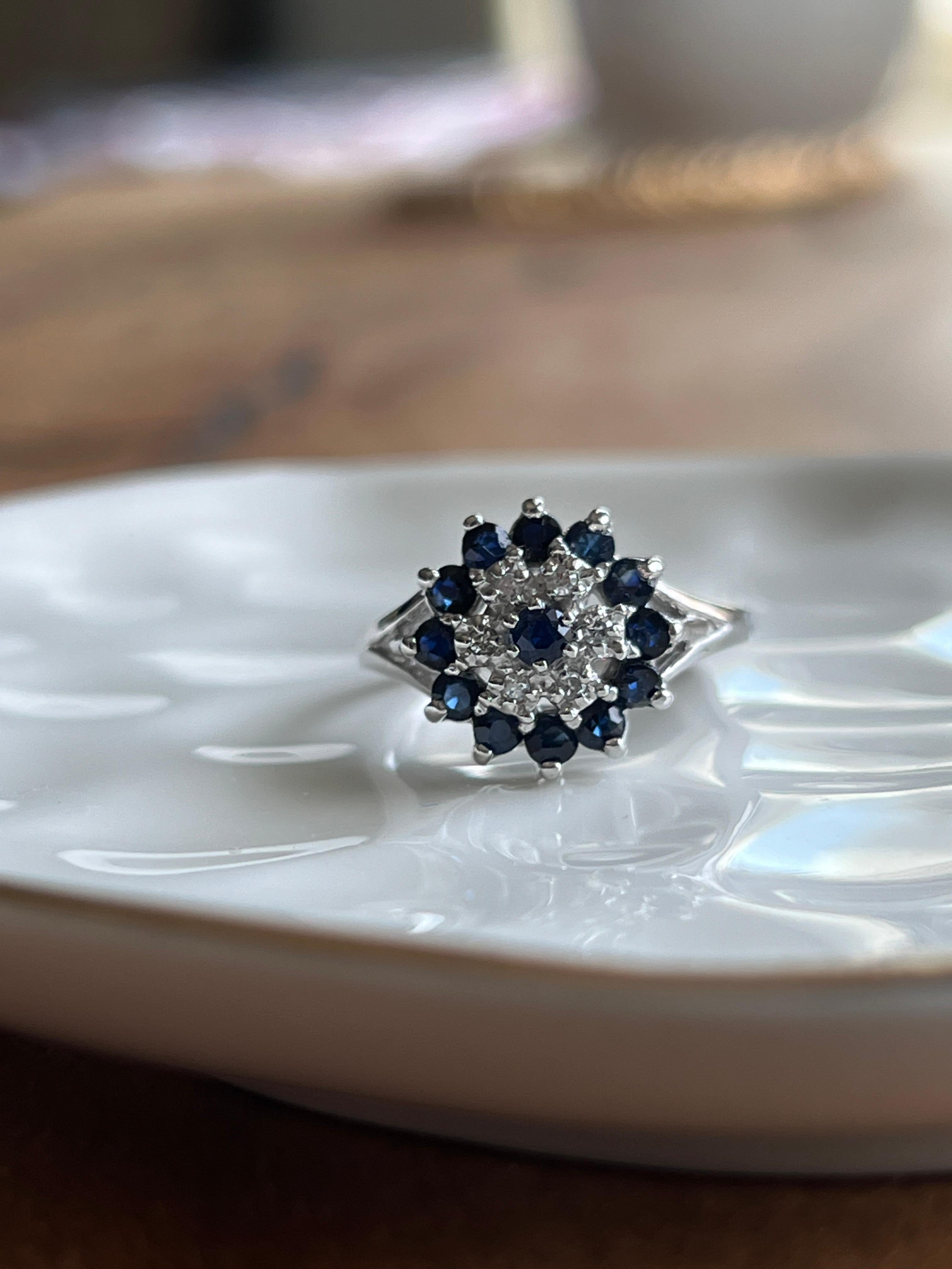 Crafted in 10 karat white gold, this elegant vintage ring showcases a sparkling arrangement of vibrant gemstones. At its center are thirteen round-cut blue sapphires, totaling approximately 0.71 carats, offering a rich, velvety hue that contrasts