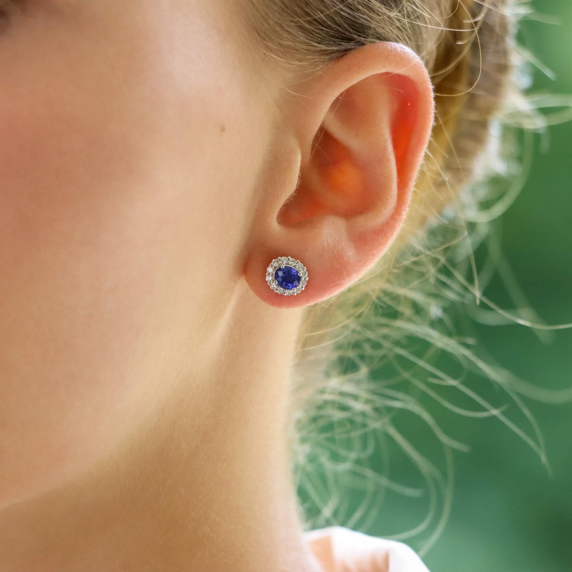  A lovely pair of sapphire and diamond oval halo earrings set in 18k white gold.

Each earring centrally features a beautiful royal blue coloured oval shaped sapphire surrounded by a halo of 12 round brilliant-cut diamonds. All of the stones are set