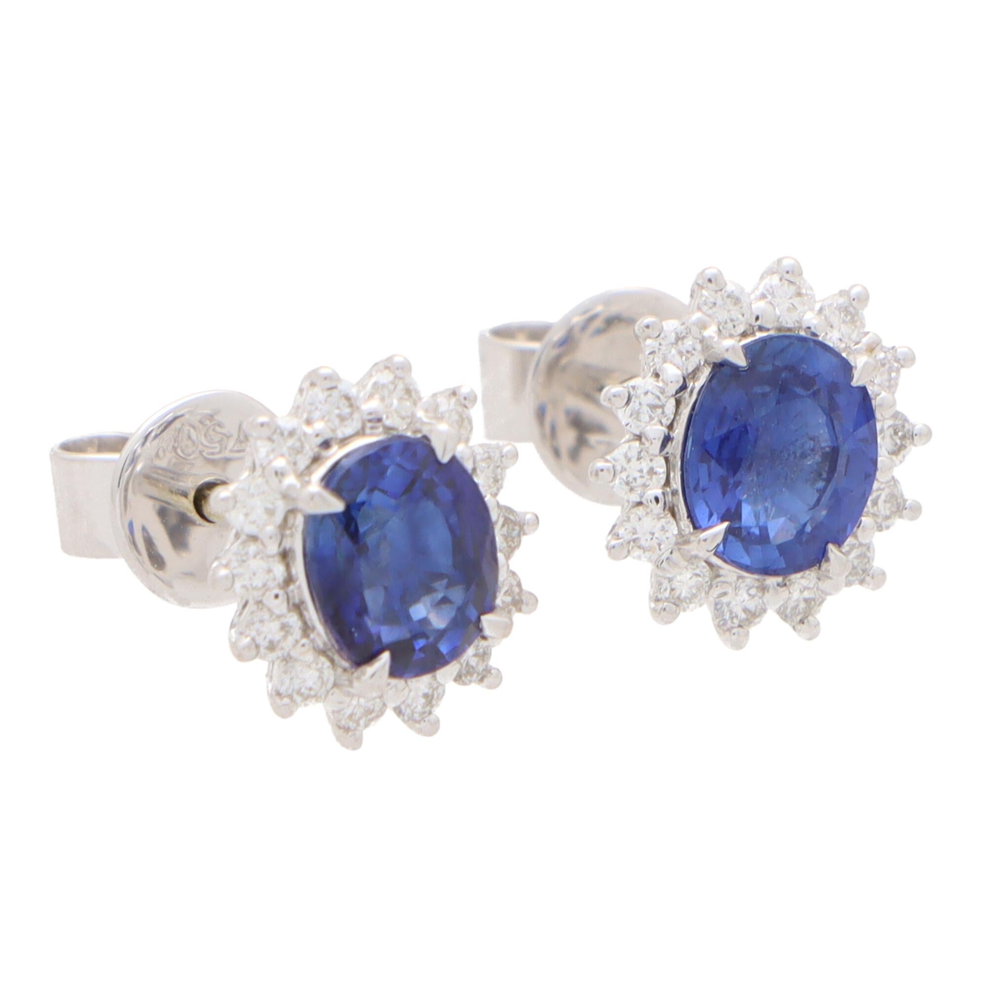 A beautiful pair of sapphire and diamond oval halo earrings set in 18k white gold.

Each earring centrally features a beautiful royal blue coloured oval shaped sapphire surrounded by a halo of 14 round brilliant-cut diamonds. All of the stones are