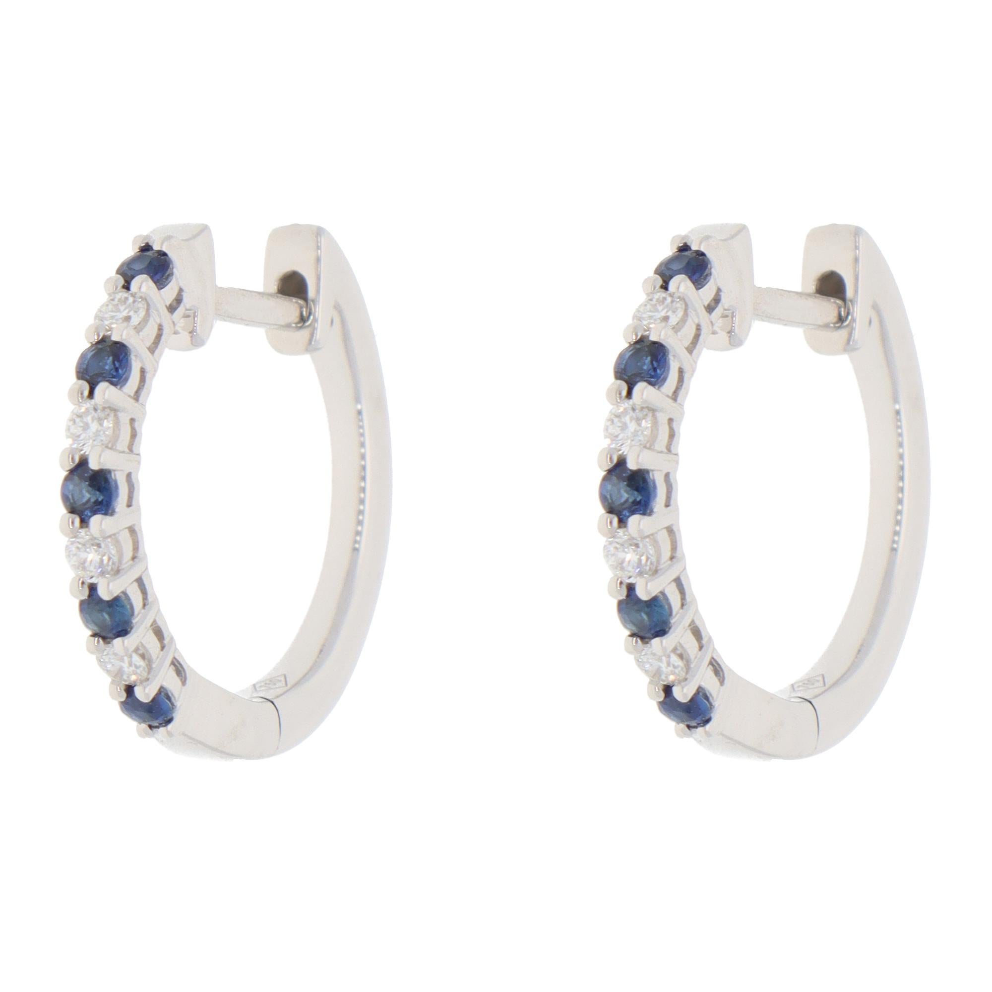A classic pair of contemporary sapphire and diamond hoop earrings set in 18k white gold.

Each earring is set with 5 vibrant sapphires and 4 round brilliant-cut diamonds. The vivid blue round sapphires are contrasted with the colourless diamond