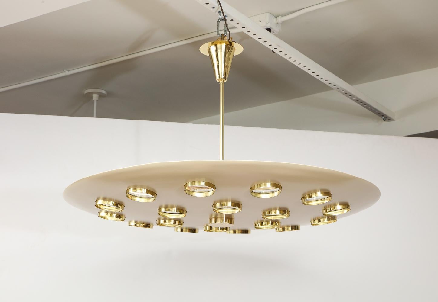 Beautiful cream-painted aluminum saucer form, with circular cut-outs. Each cut-out is fitted with a brass framed glass lens, creating a subtle abstract effect. 6 candelabra sockets and polished brass mounts. The rod can be cut down and this light