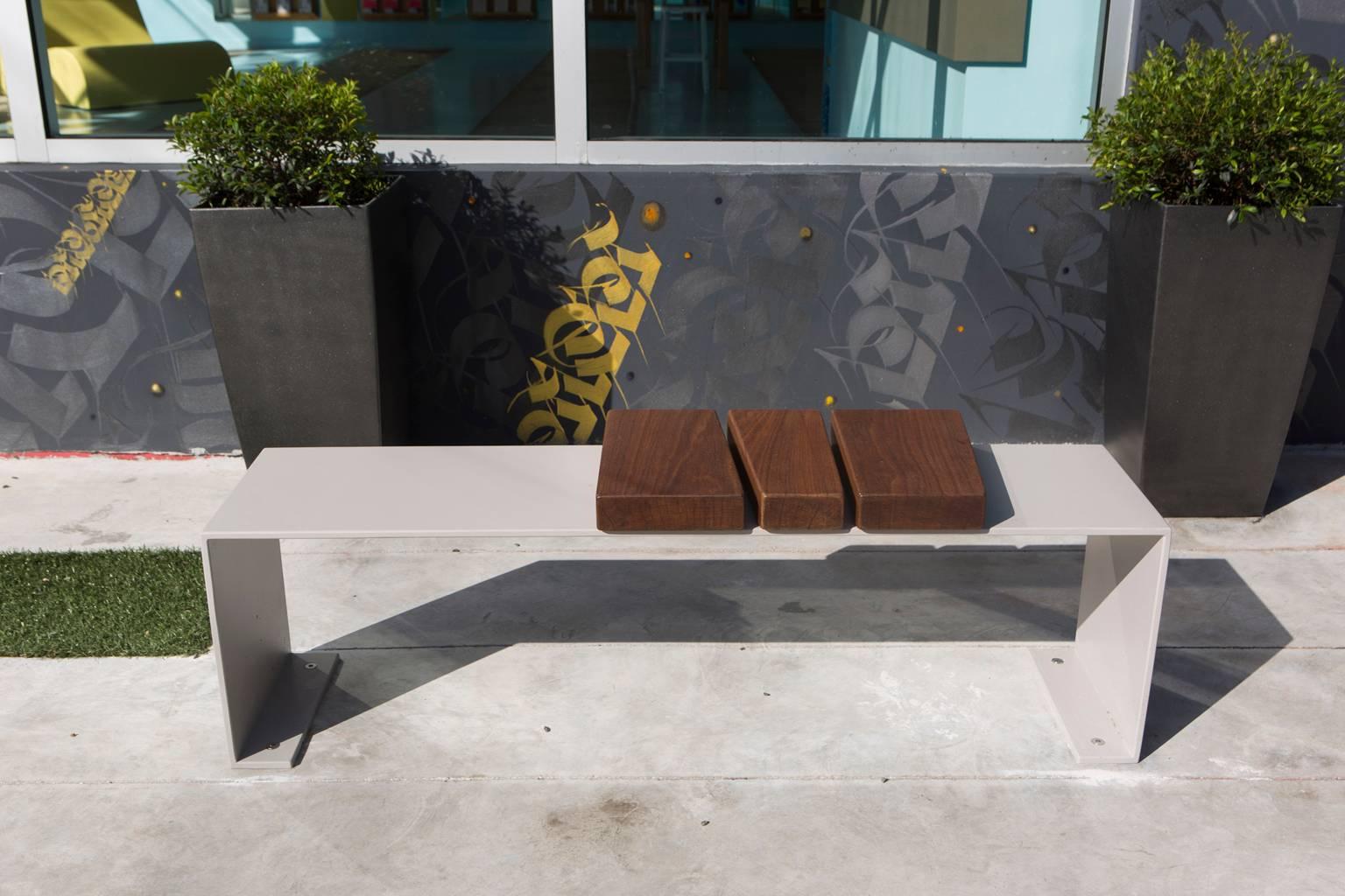 This bench design was originally commissioned for an exterior public art space in Wynwood, Florida. It is shown here in aluminum with a flat grey powder coated finish and solid Ipe wood. It is also available in various powder coating colors. The