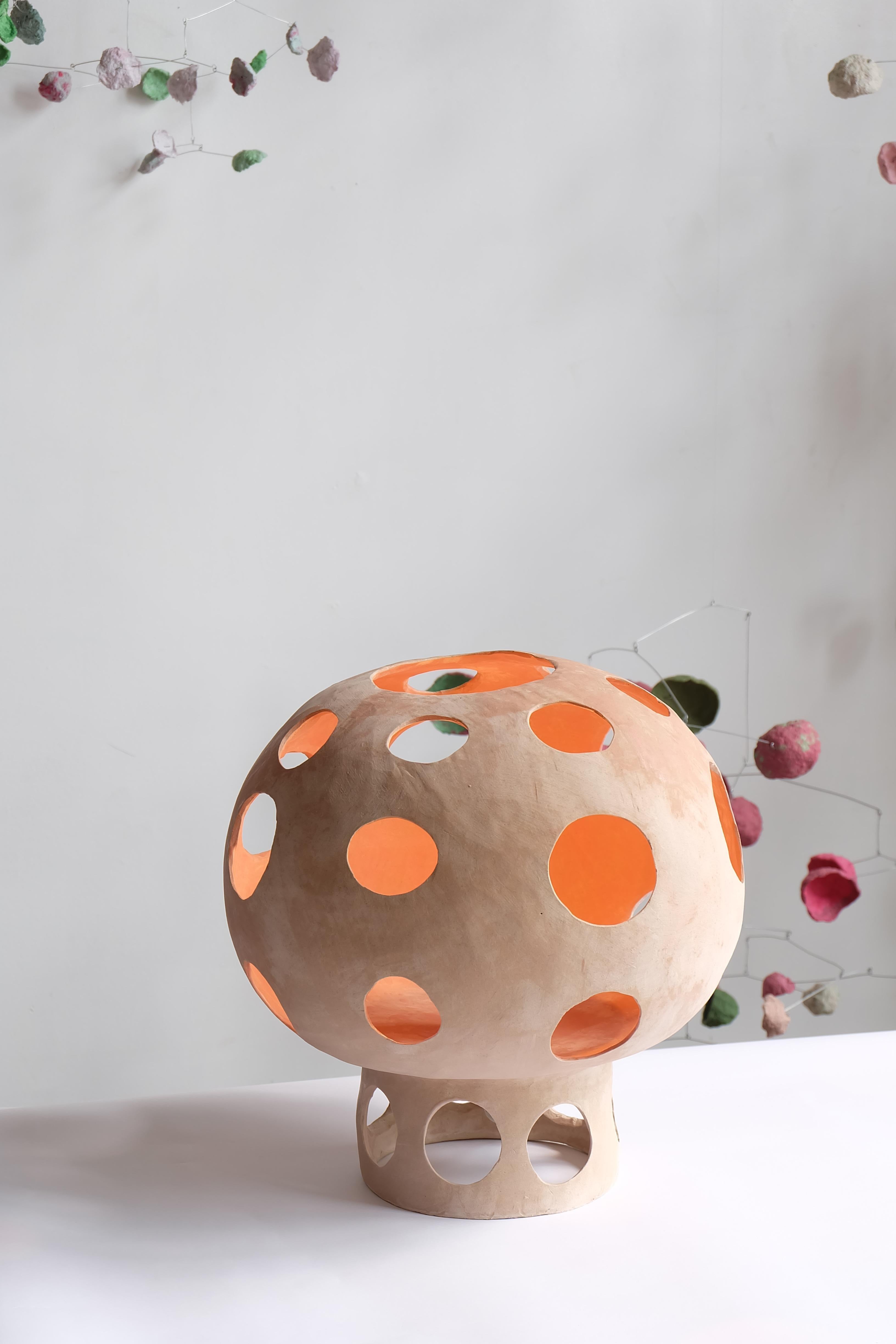 Persimmon is a mushroom-shaped hand-built ceramic table lamp whose plinth base and socket cover are integrated into the main body making one seamless sculptural ceramic shell. The cutouts on the body add character and project multiple round spots of