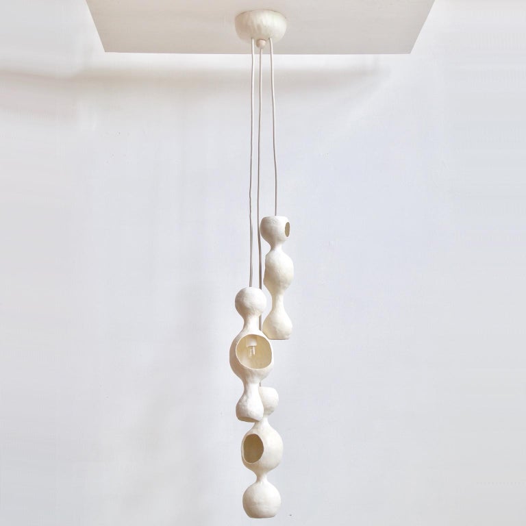 White bowerbird family is a contemporary sculptural multi-shell hand-built ceramic pendant lamp finished in a matte white glaze with a warm glow reflecting off of a round joyful form. Each shell is individually hand formed and unique, creating a