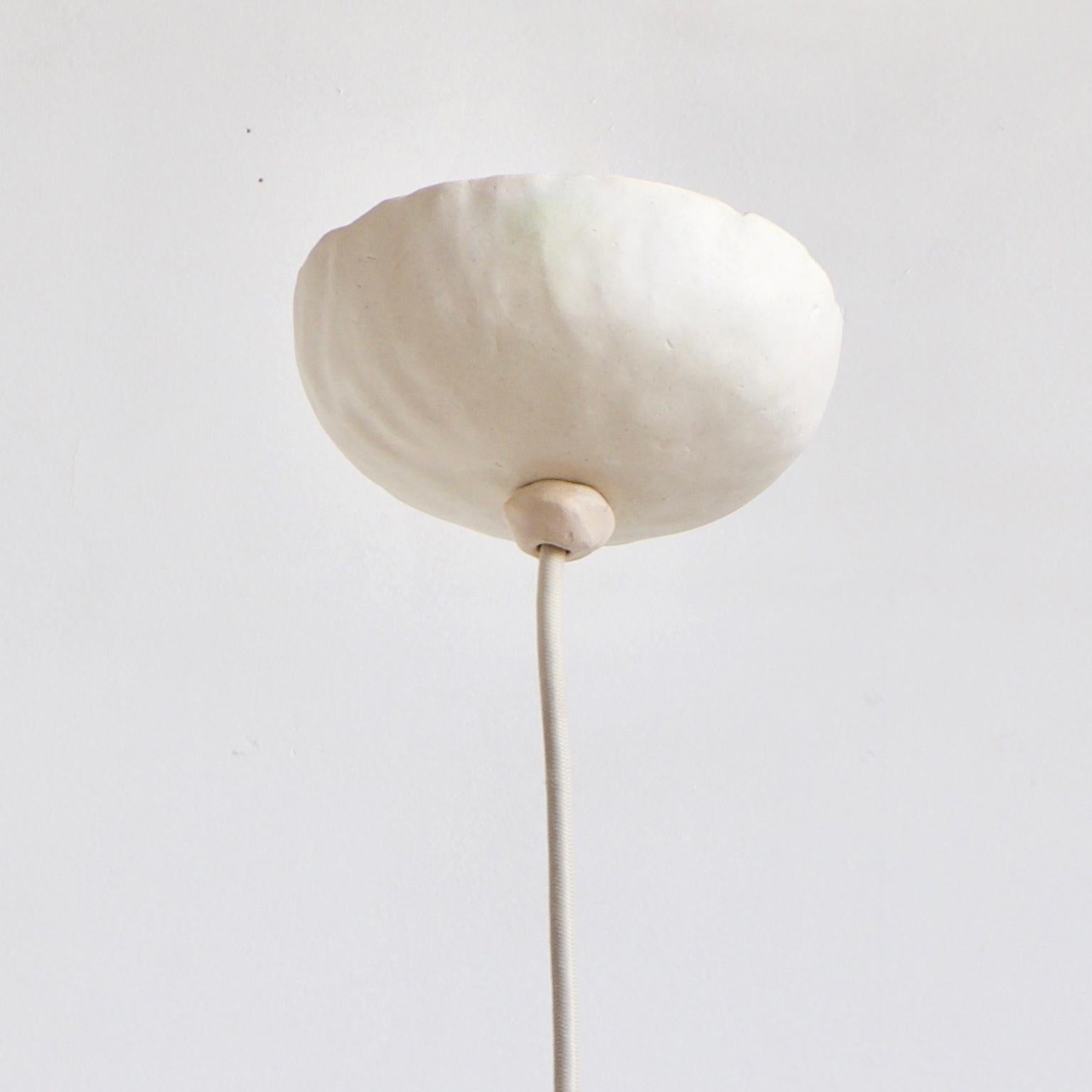 White Bowerbird single ist eine zeitgenössische, handgefertigte Hängeleuchte aus Keramik in mattweißer Glasur mit einem warmen Licht, das von einer runden, fröhlichen Form reflektiert wird. Die humorvolle, freundliche Form setzt einen spielerischen