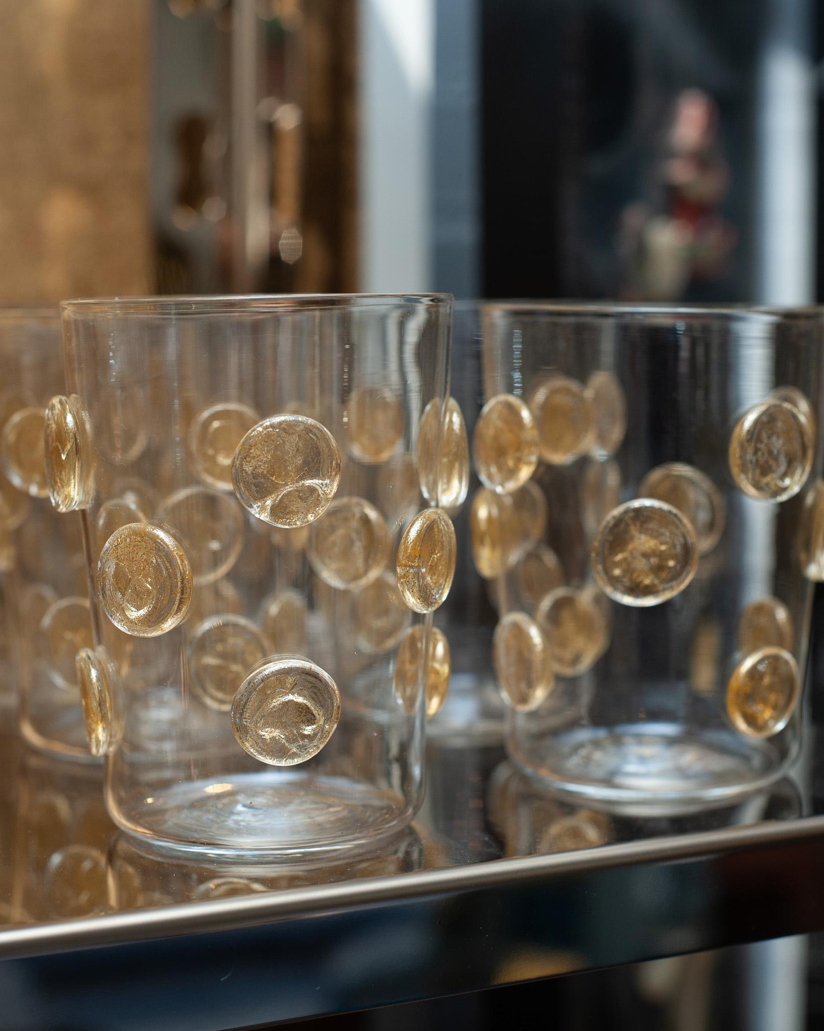 A contemporary set of 12 Murano spotted tumblers with gold leaf by a Venetian master glass blower. Each glass is thin and beautifully crafted with gold leaf spots. Made in Murano, they are true jewelry for the table.