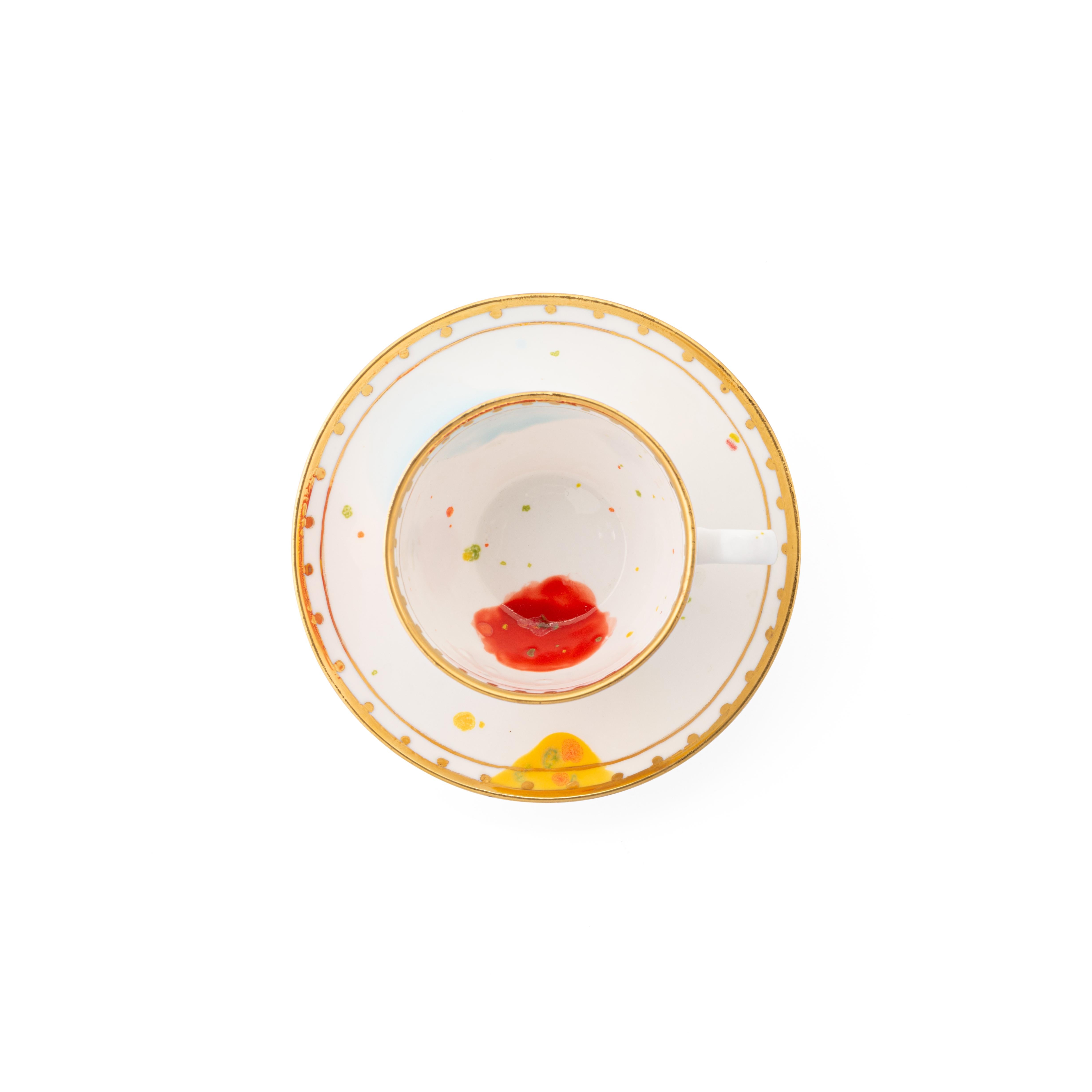 Handcrafted in Italy from the finest porcelain, this Caravaggio tea cup and saucer is painted both inside and outside with red, yellow and light-blue splotches on a white enamel; an elegant golden rim turns inside like a medieval tower battlements