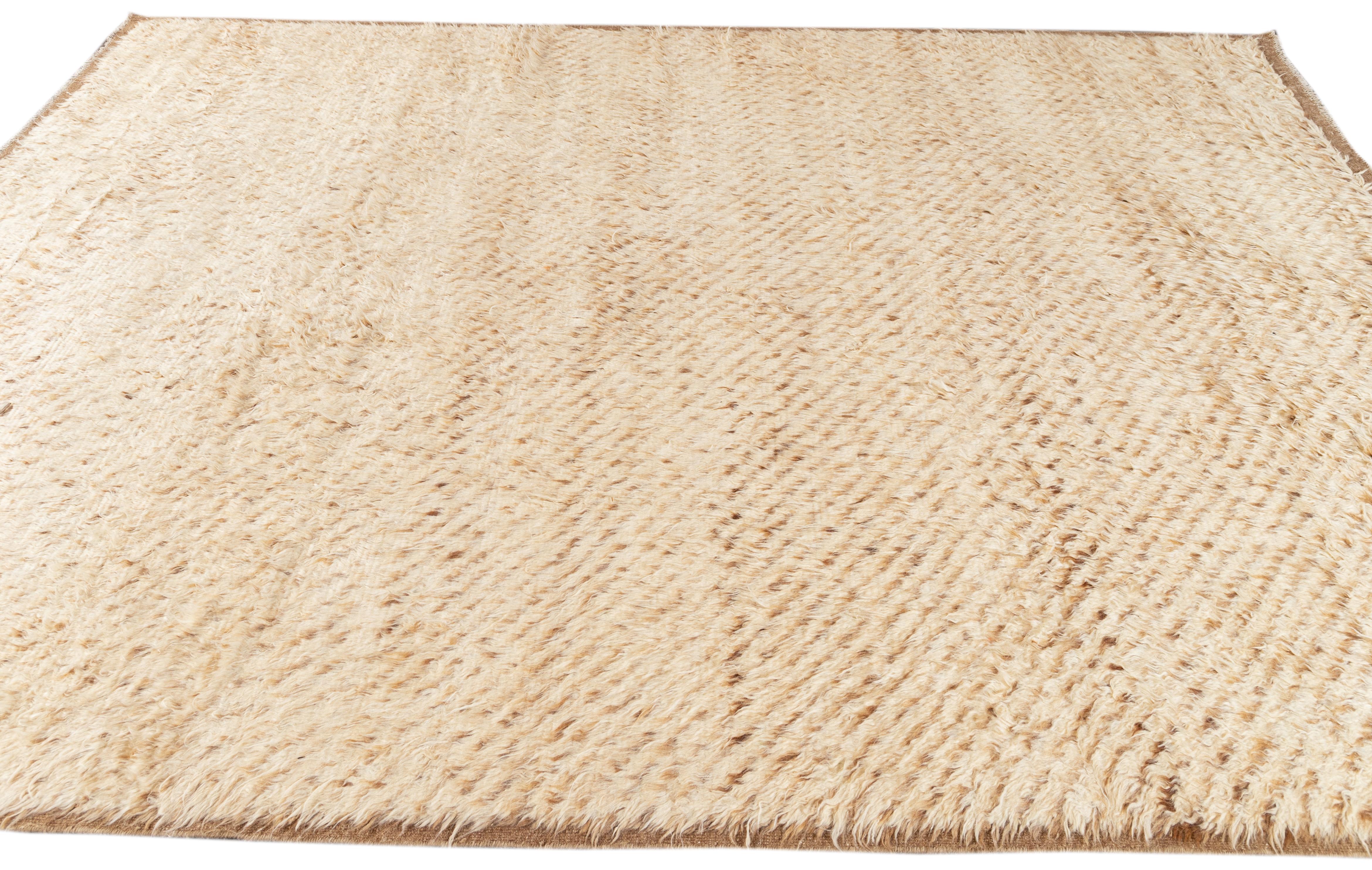 This hand-knotted wool rug showcases a stunning contemporary Moroccan style. It boasts a beautifully plain design, with a tan field and a brown frame. Crafted with utmost precision, this shag rug is a masterpiece that adds a touch of sophistication
