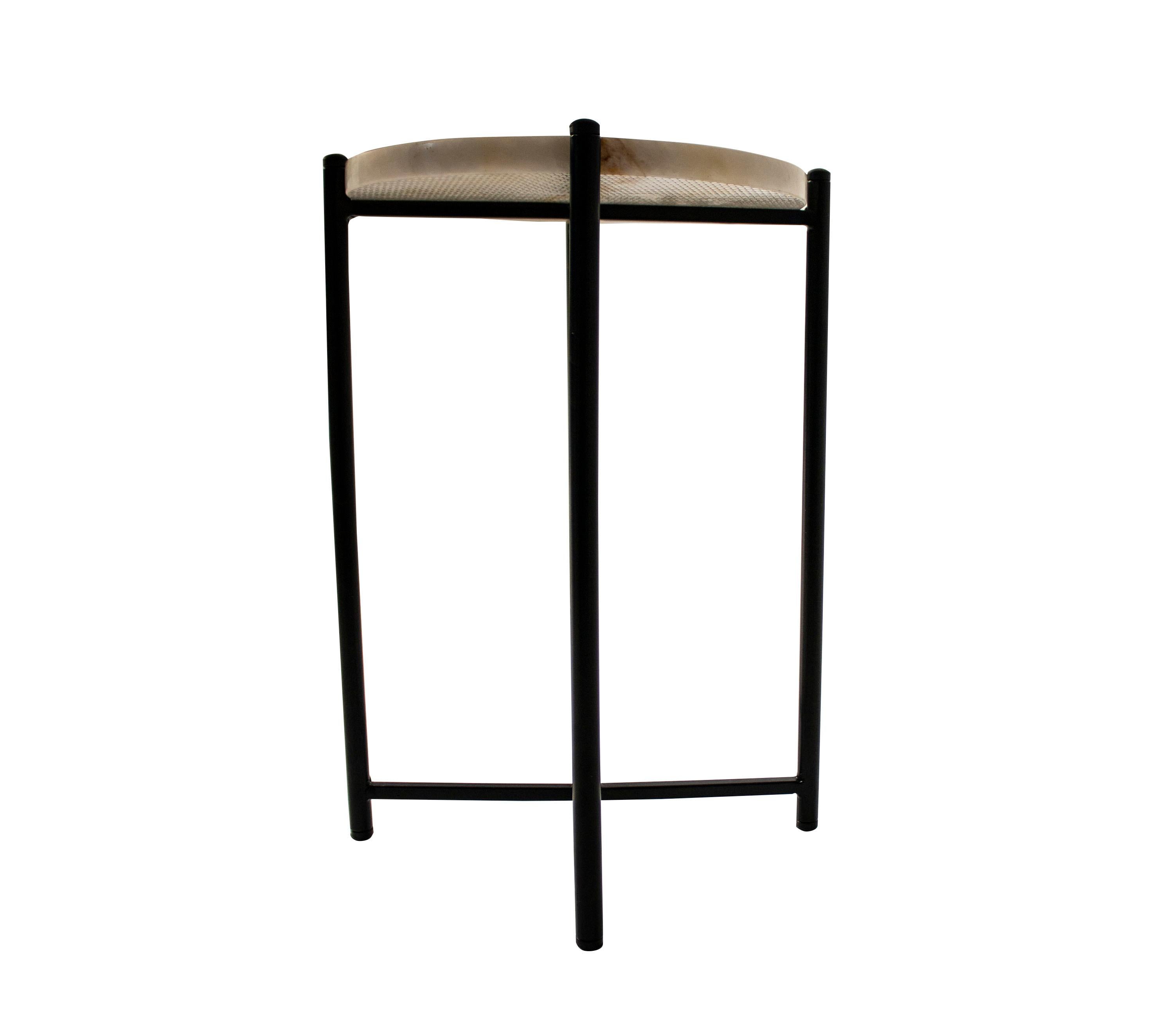 Table with an X-shaped base and a black lacquered iron structure that protrudes a few millimeters from its surface. 
The round top is carved from white onyx with an ocher beta.