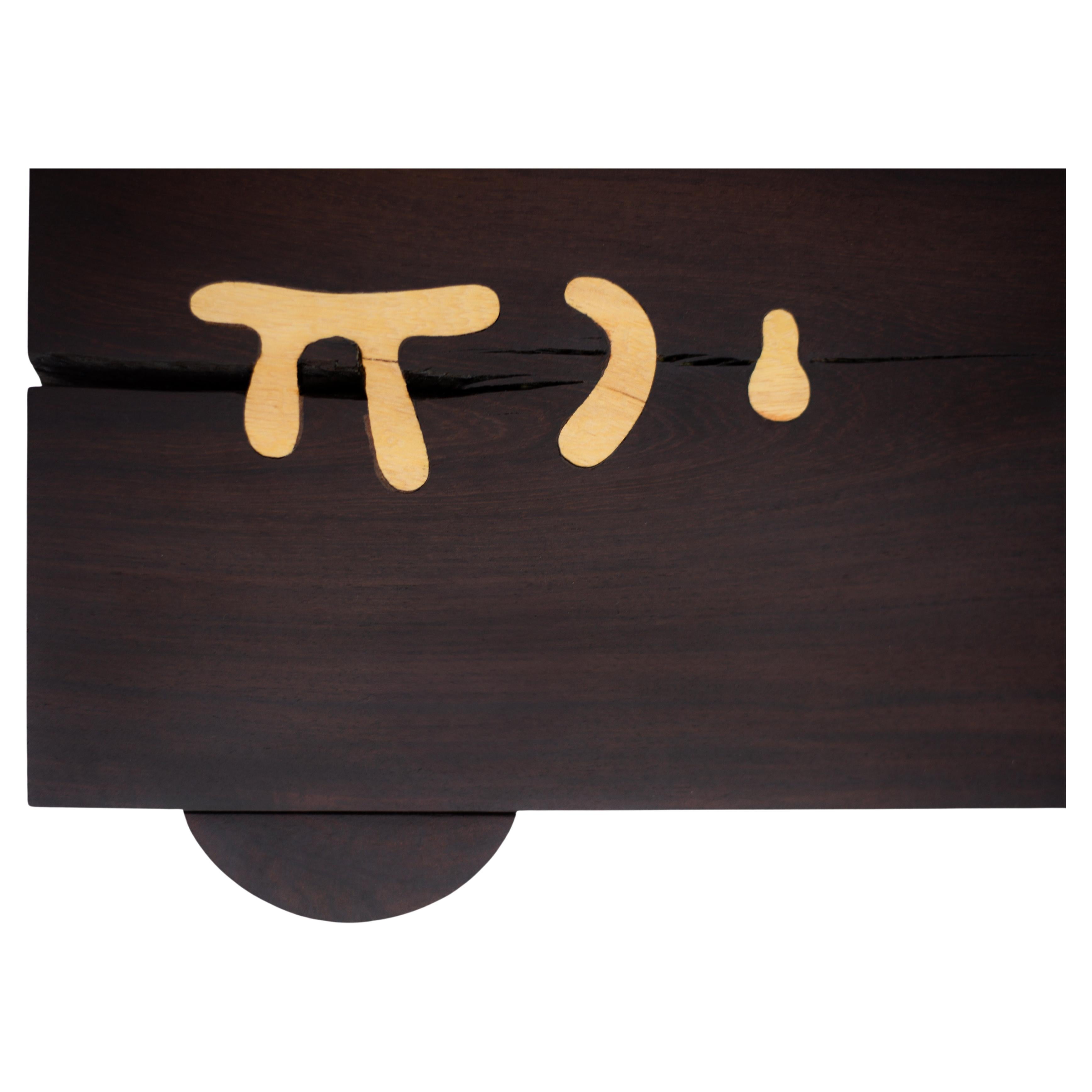 The tabletop planks feature small cracks and fissures, thoughtfully intervened with inlaid symbols that evoke ancient scripts and universal archetypes. These marks are not decorative elements, but gestures of connection—carefully placed after