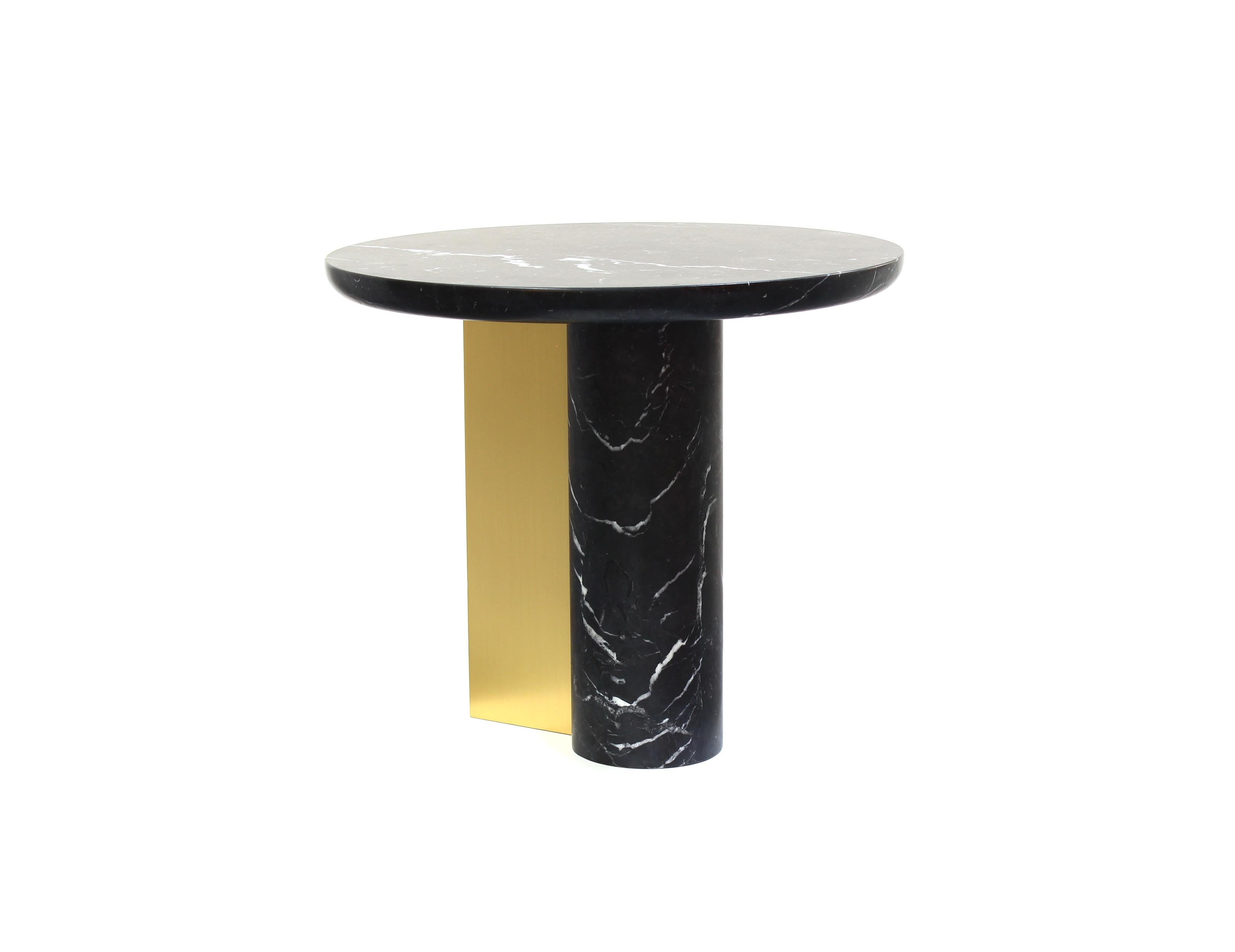 This monolithic side table has an elegant and refined silhouette. An off-balanced cylindrical solid base attached to a circular top is supported by a folded brass plate enlightening and balancing the piece.
The simple elegance of essential forms