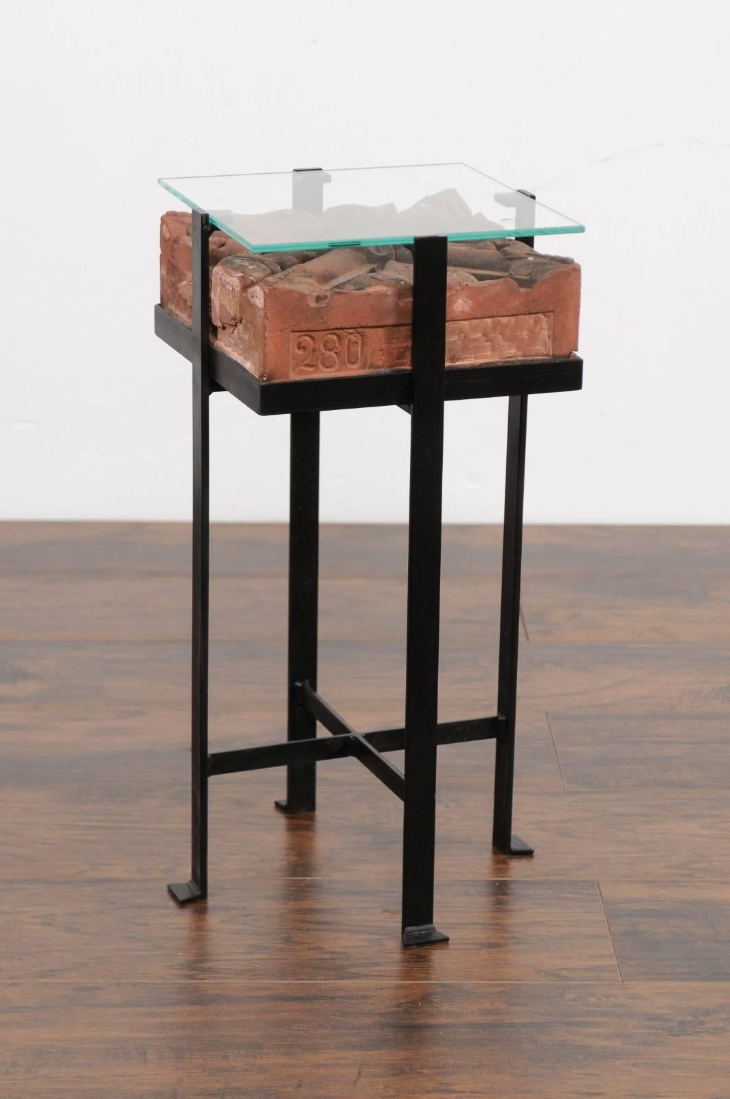 A contemporary side table made of an Italian antique red brick from the early 20th century with glass top and custom iron base. This small side table features a square top made of an antique Italian red brick from the 1900s, adorned with a