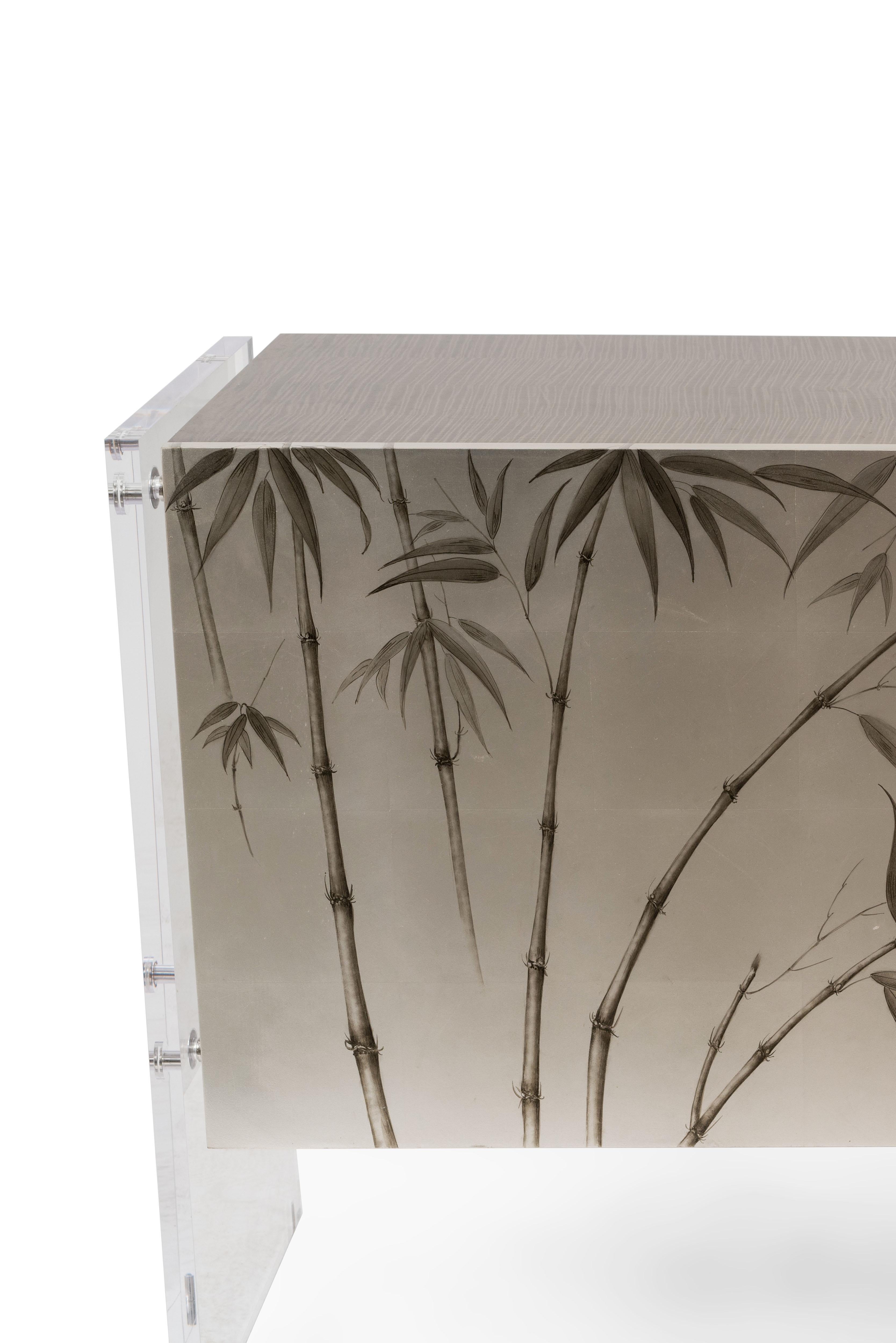 Contemporary silver/gray painted commode with bamboo floral design on the front doors and a gray wood veneer finished top. Sides supported on solid Lucite panels with silver metal detail. (THEODORE ALEXANDER).