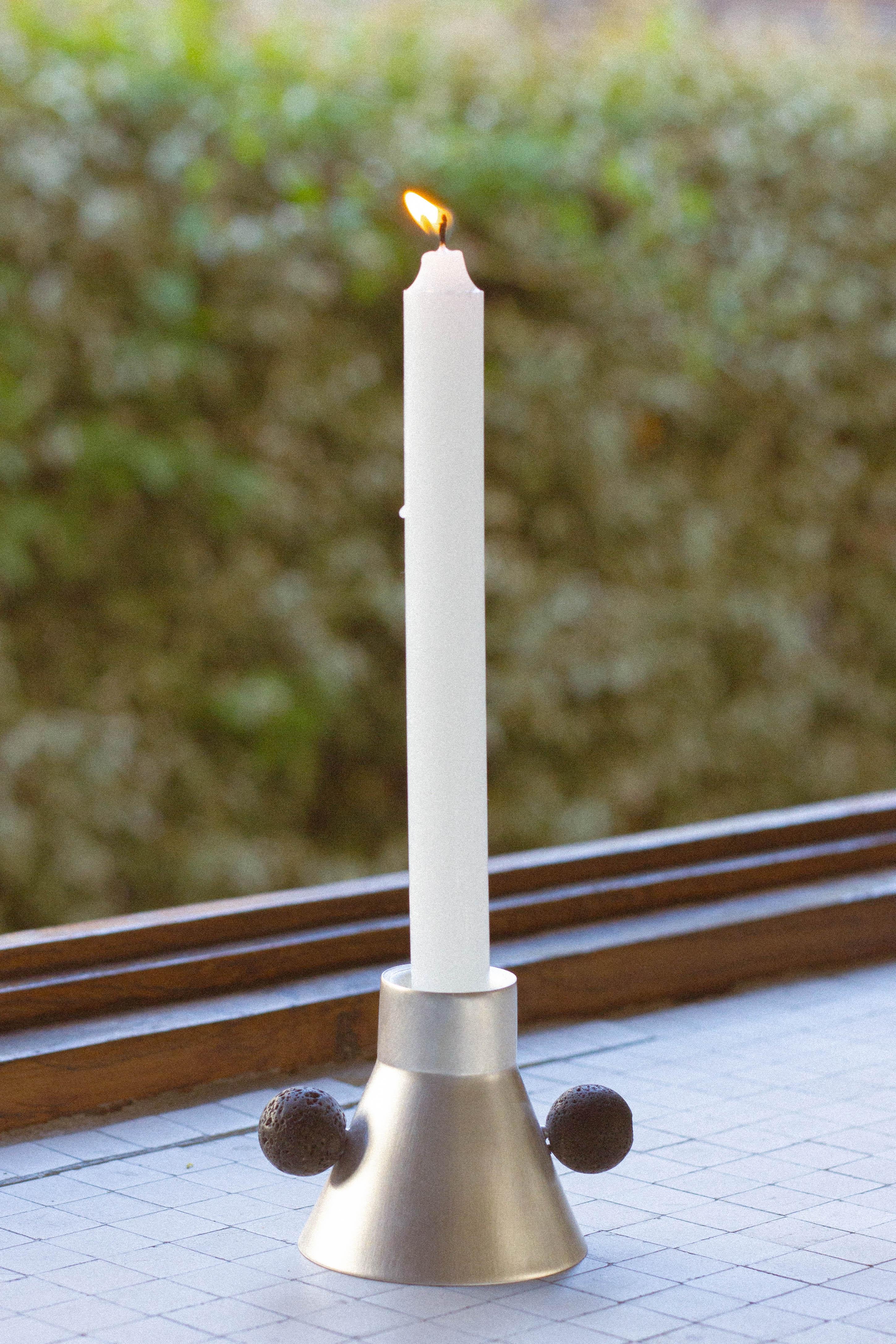 Elevate your daily rituals with our exquisite candle holder. Meticulously handcrafted with plated brass, its geometric silhouette tapers at the top for a sleek and minimal aesthetic. The refined stone handle in lava rock introduces a touch of