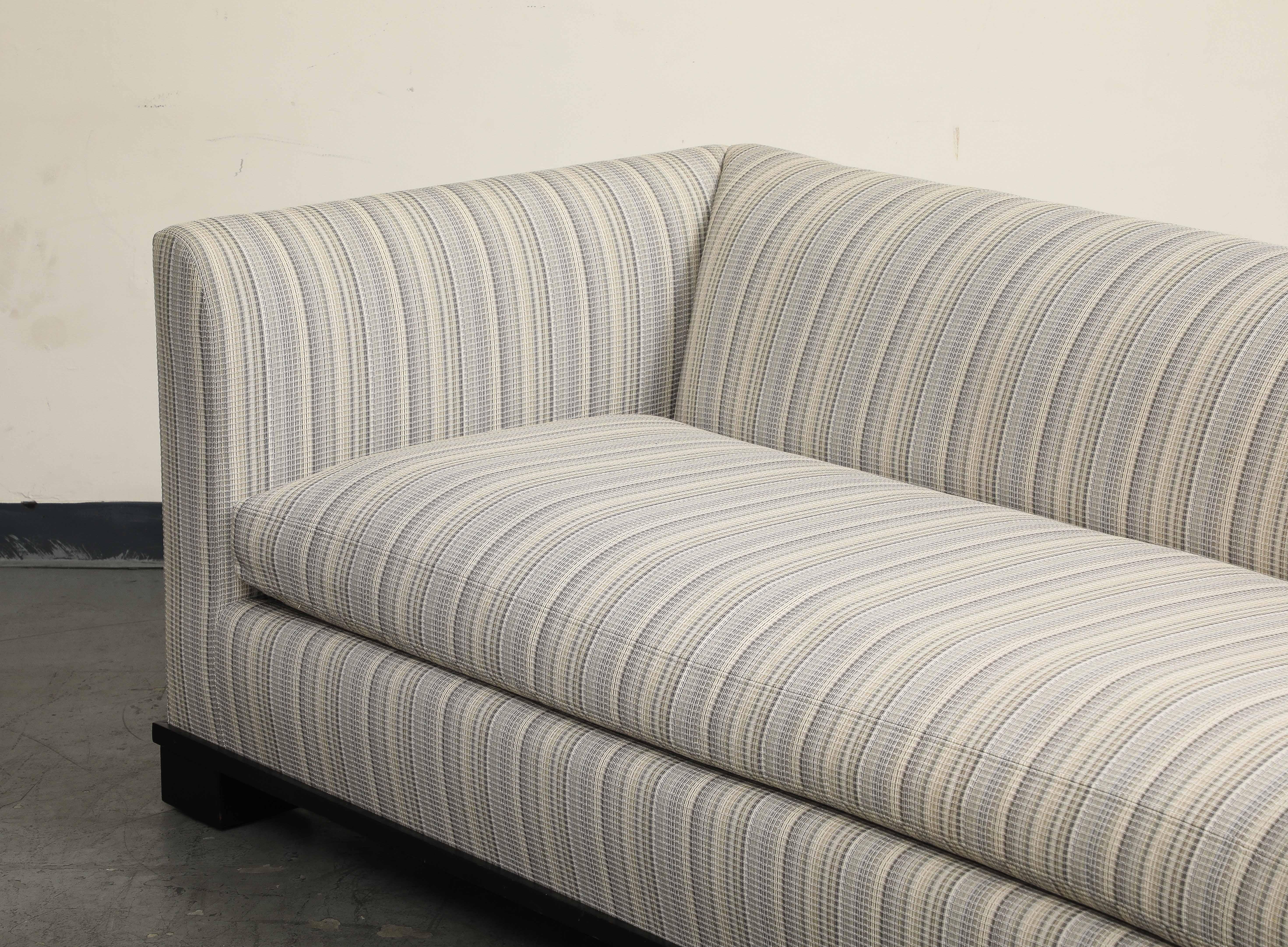 Contemporary single-cushion sofa upholstered in purple, blues and cream stripes, resting on block feet and wood base. 