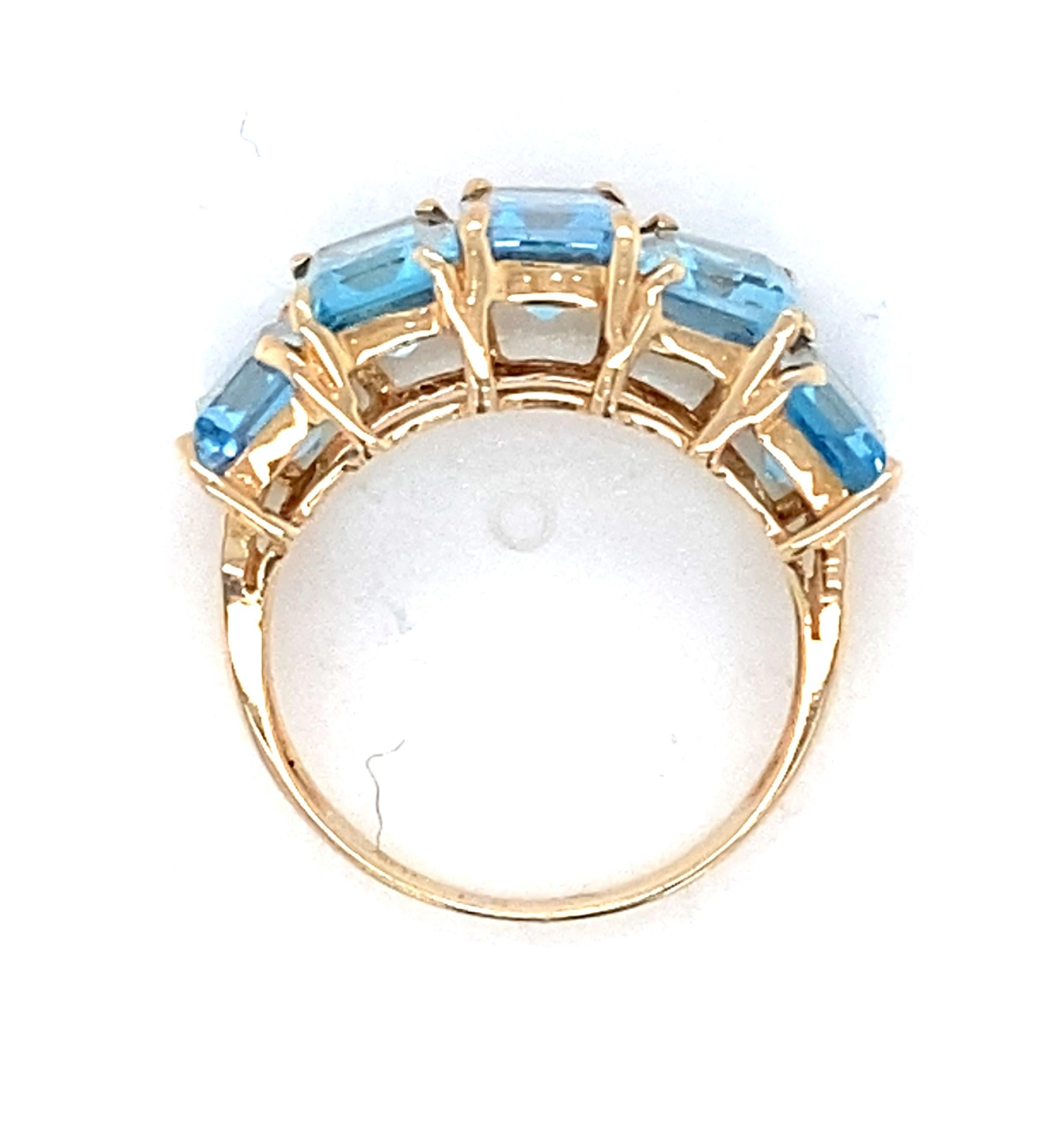 This 10 karat yellow gold ring features five equally sized sky blue rectangular step-cut topaz, weighing approximately 5.95 carat total, that are prong set and step down in relation to each other with the center topaz flanked on each side by two
