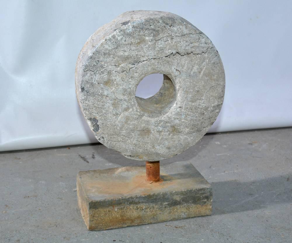 The vintage small millstone sculpture is attached by an iron rod to a stone brick-shaped base.  The piece has a decidedly contemporary modern look that will make a wonderful statement in any setting.  The stone itself measures approximately 8