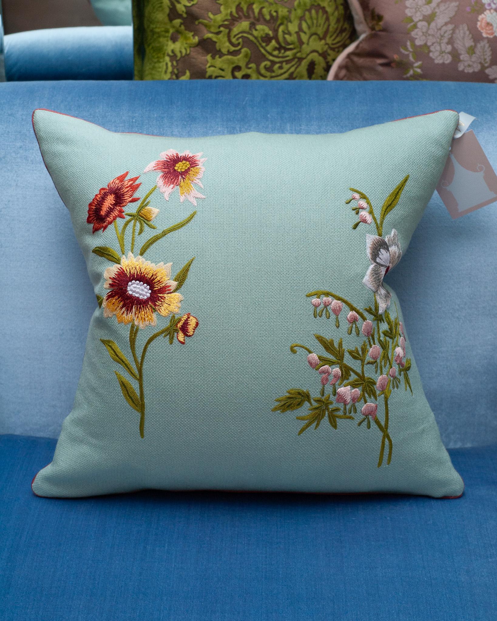 A stunning contemporary soft blue merino wool and linen pillow, trimmed with red piping and embroidered in wool with double floral motifs. Filled with the highest quality Canadian down and feather for a pillow that feels as luxurious as it is